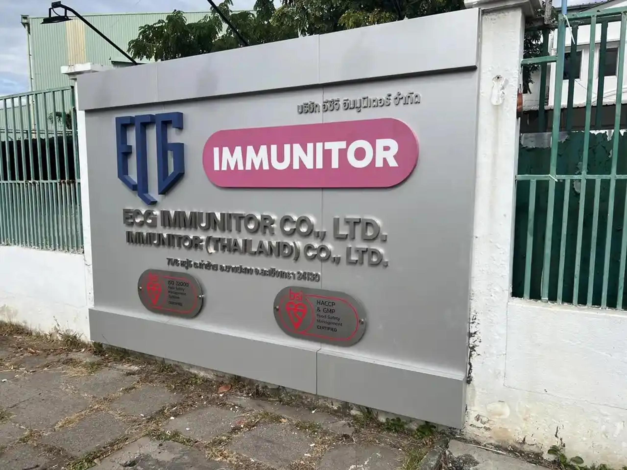 ป้ายชื่อบริษัท ECG Immunitor Co., Ltd. ติดผนังรั้วหน้าอาคาร มุมมองใกล้ | Close-up view of the ECG Immunitor Co., Ltd. company name sign on a front wall