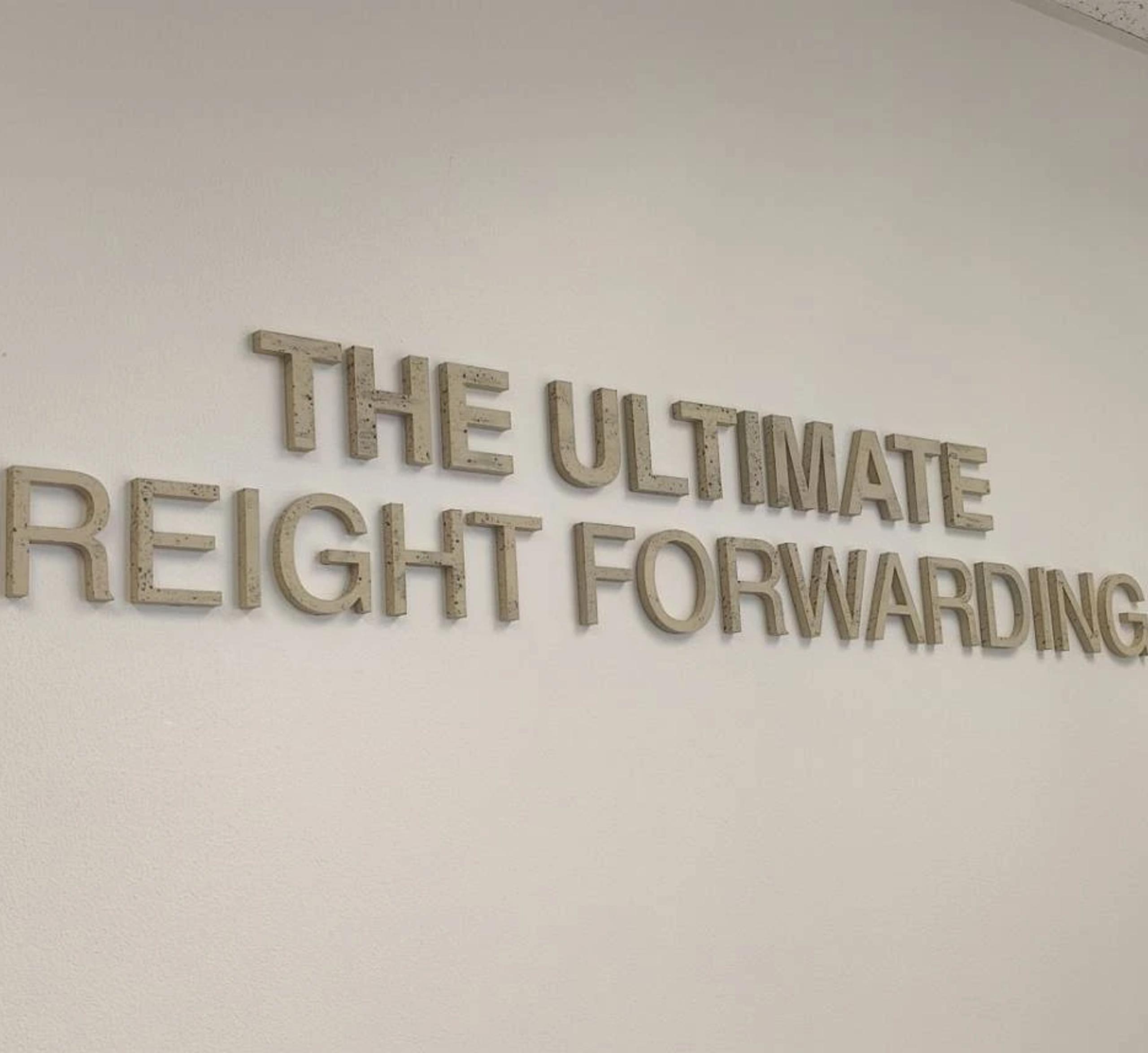ป้ายตัวอักษรโลหะไม่มีไฟข้อความ THE ULTIMATE FREIGHT FORWARDING ติดผนังภายในสำนักงาน