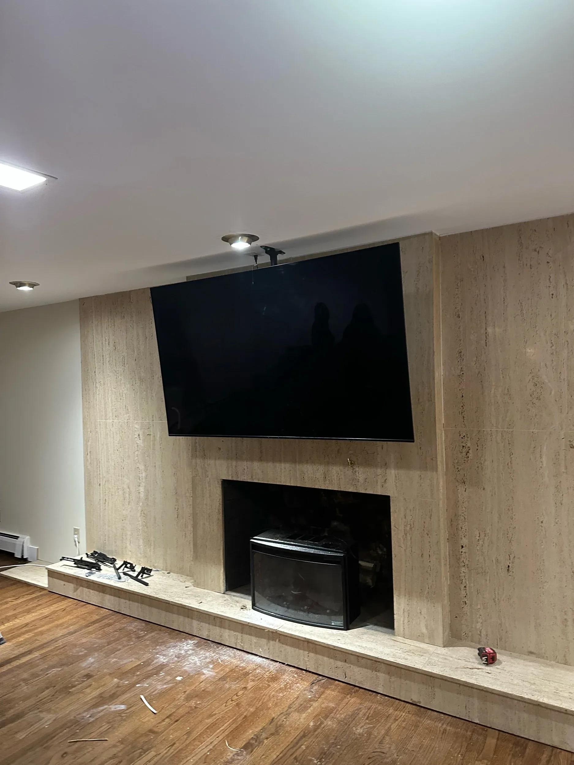 Large flat-screen TV wall-mounted above travertine fireplace with black wood stove insert and hardwood floor