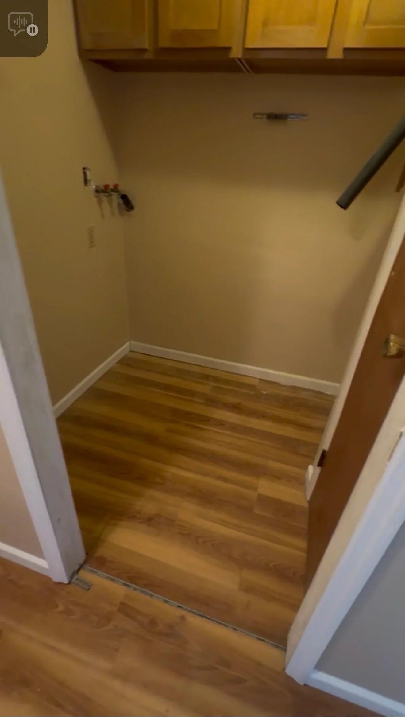 Utility closet with new wood-look vinyl flooring and beige walls under wooden cabinets