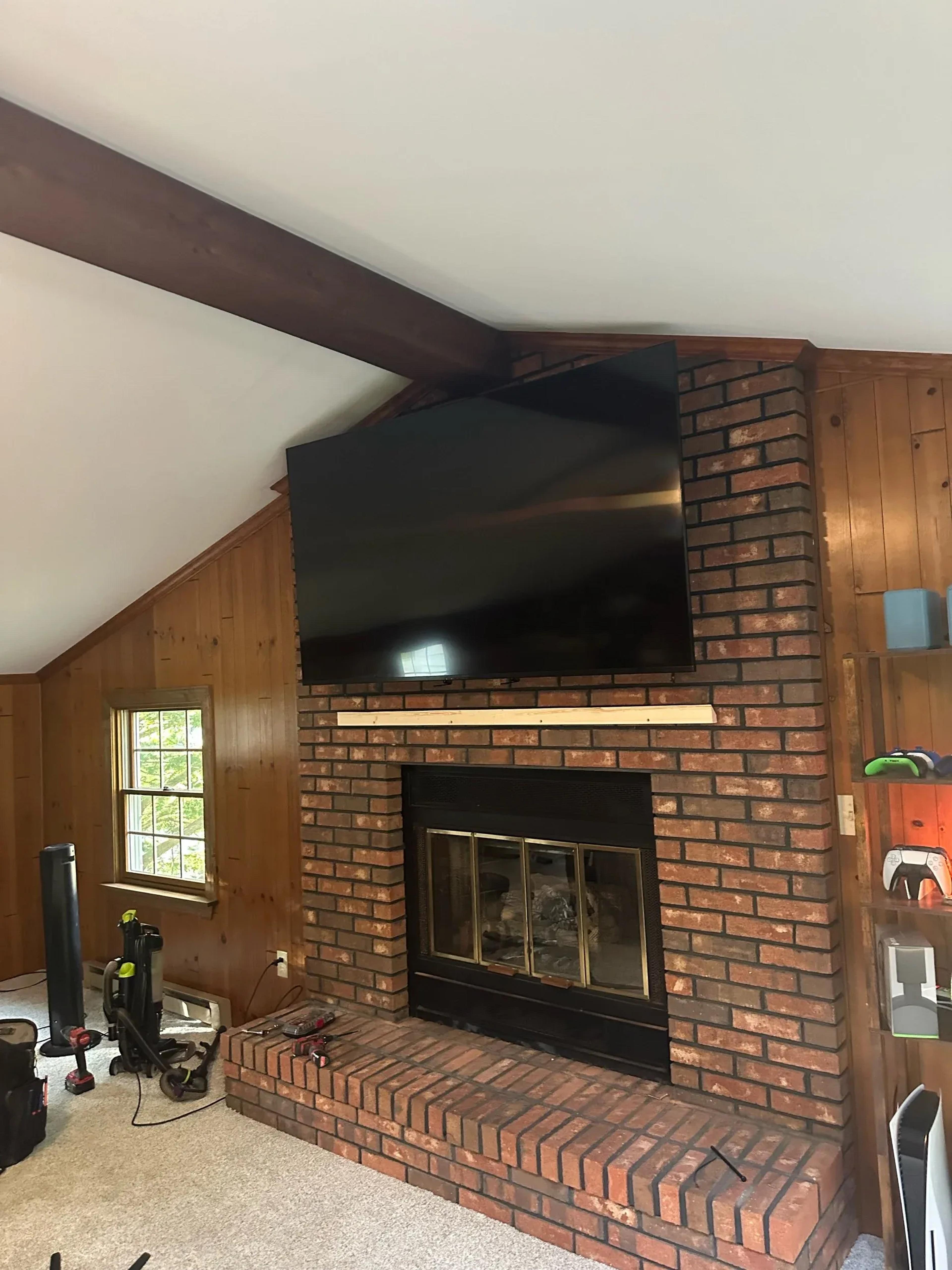 Flat-screen TV mounted above brick fireplace with angled vaulted ceiling and wood paneling walls