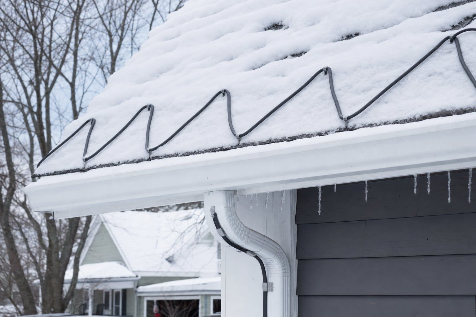 Snow-covered roof edge with a heat cable installed in a zigzag pattern along the eave and through the gutter