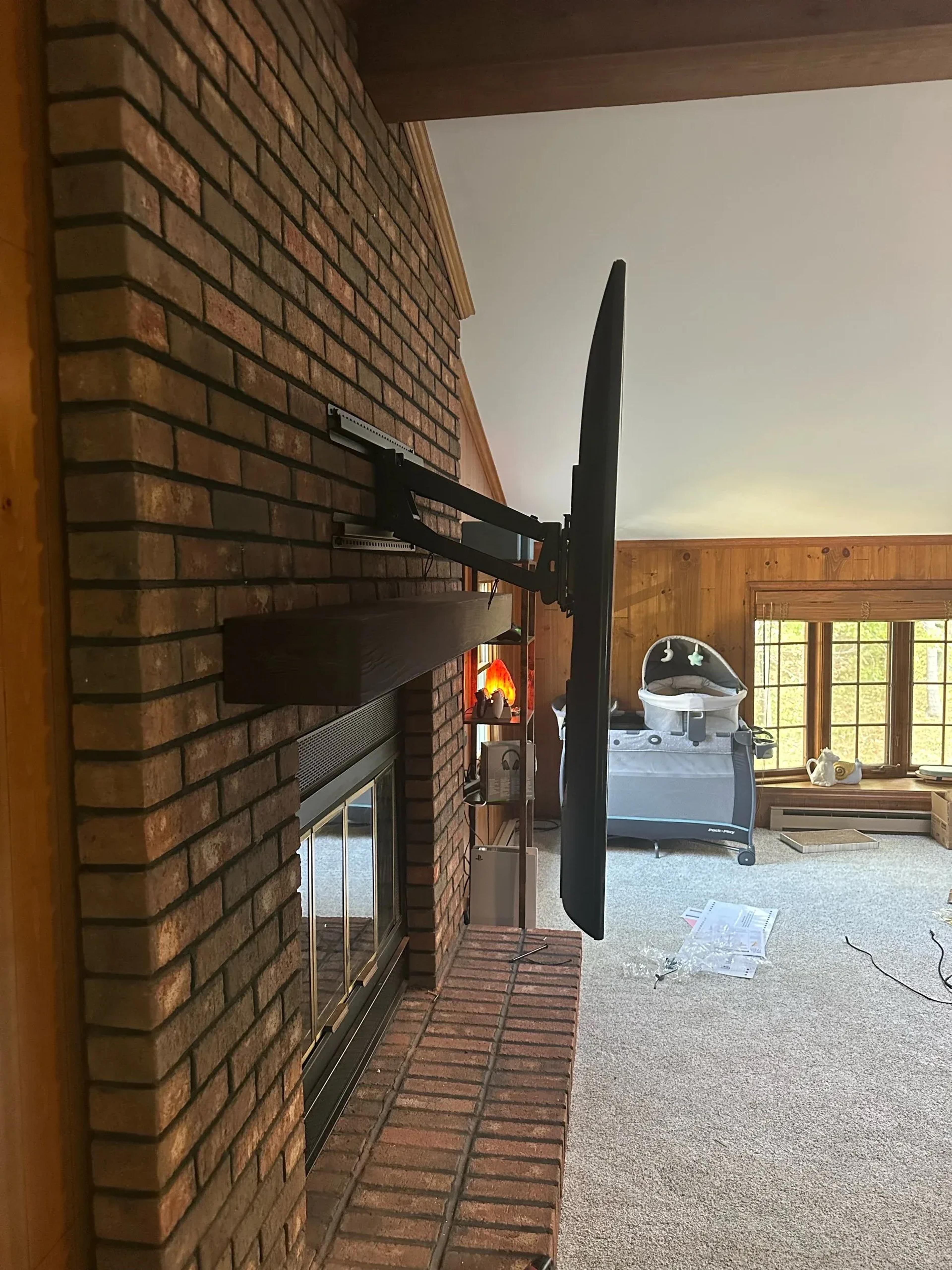 Flat-screen TV mounted on an extendable arm bracket swung out from a brick fireplace wall in a living room with baby