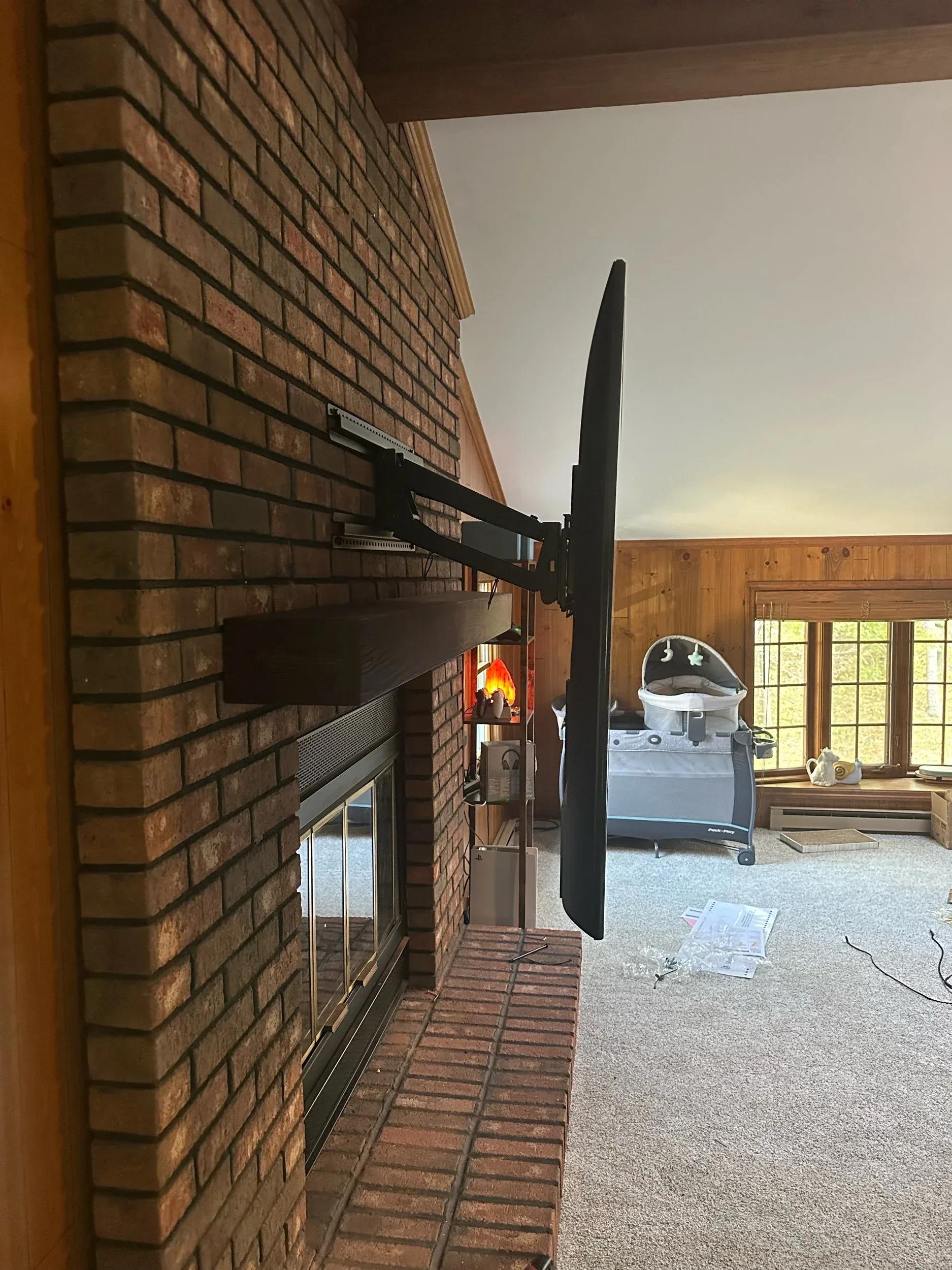 Flat-screen TV mounted on an extendable arm bracket swung out from a brick fireplace wall in a living room with baby