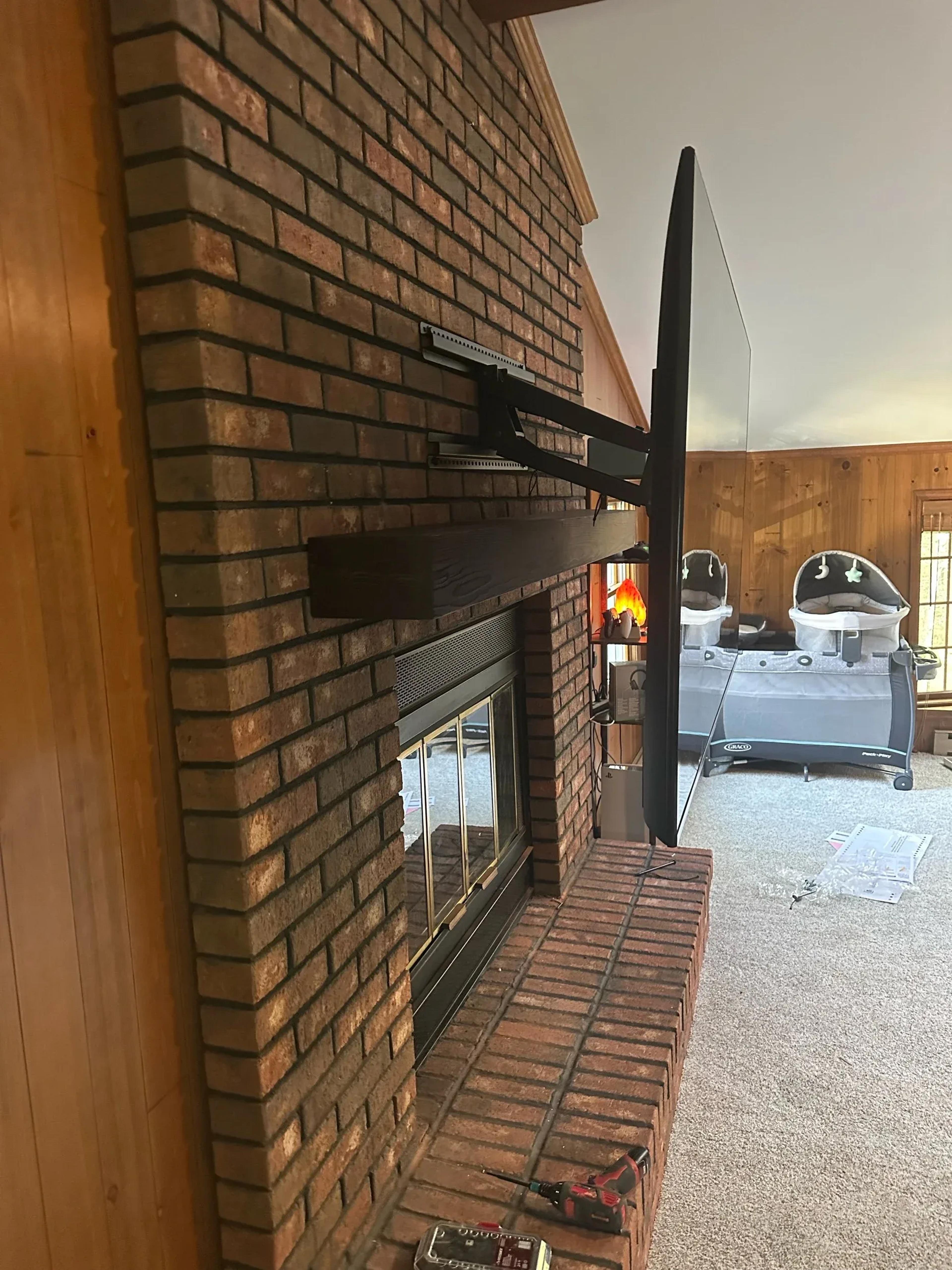 Flat-screen TV mounted on an articulating arm above a brick fireplace with wooden mantel and twin bassinets in background