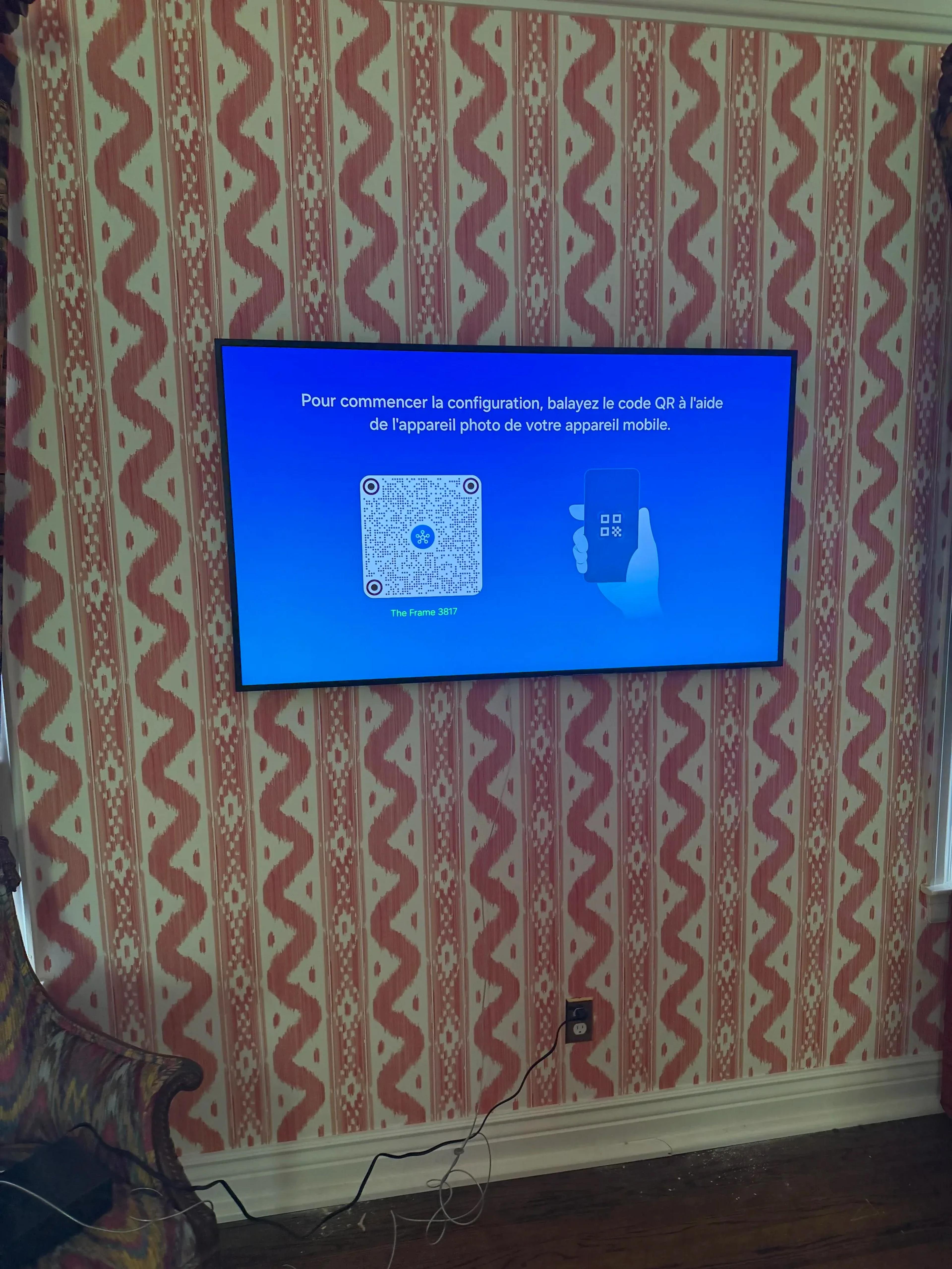 Wall-mounted flat screen TV displaying setup instructions on patterned red and white wallpapered living room wall