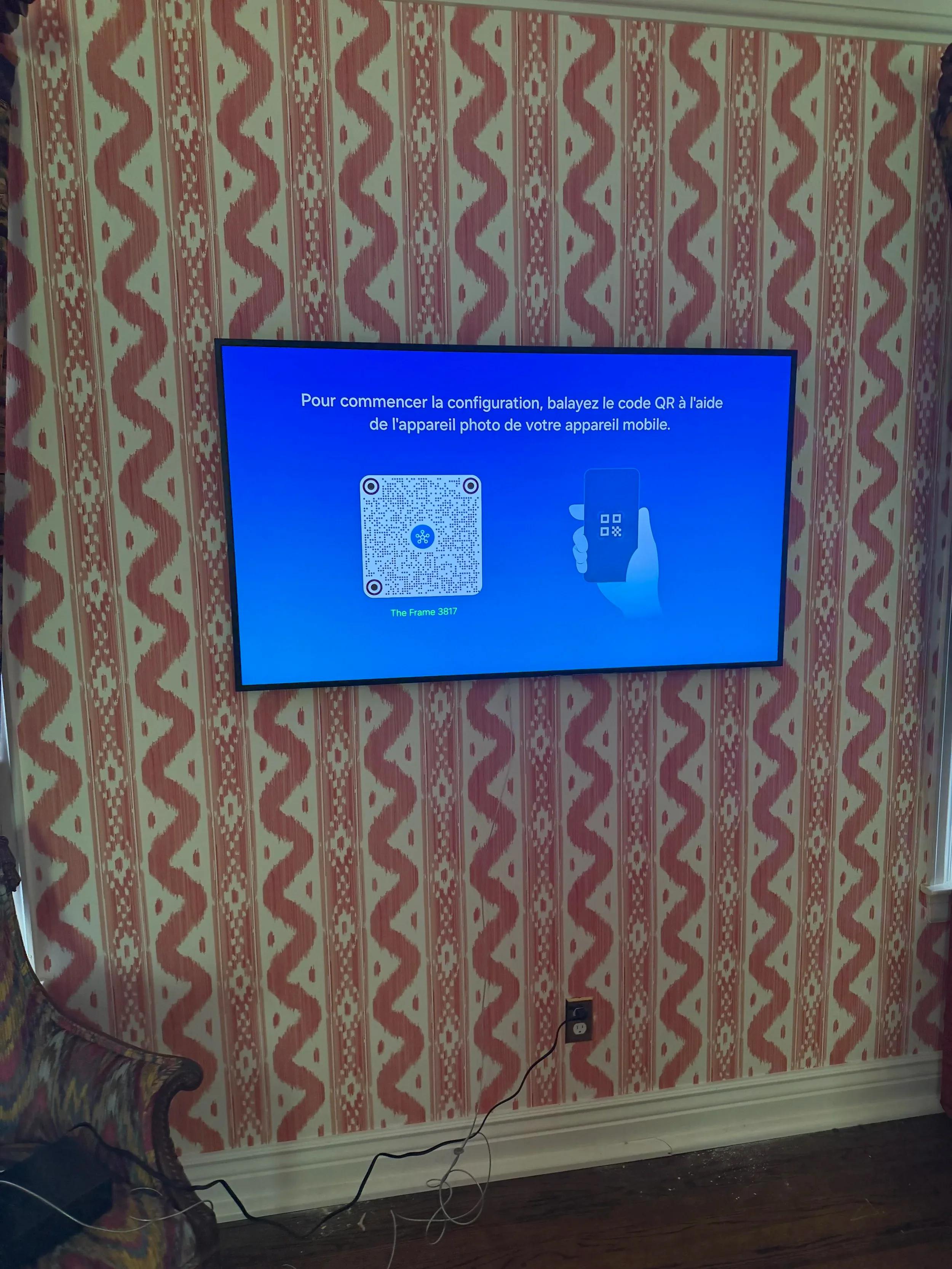 Wall-mounted flat screen TV displaying setup instructions on patterned red and white wallpapered living room wall