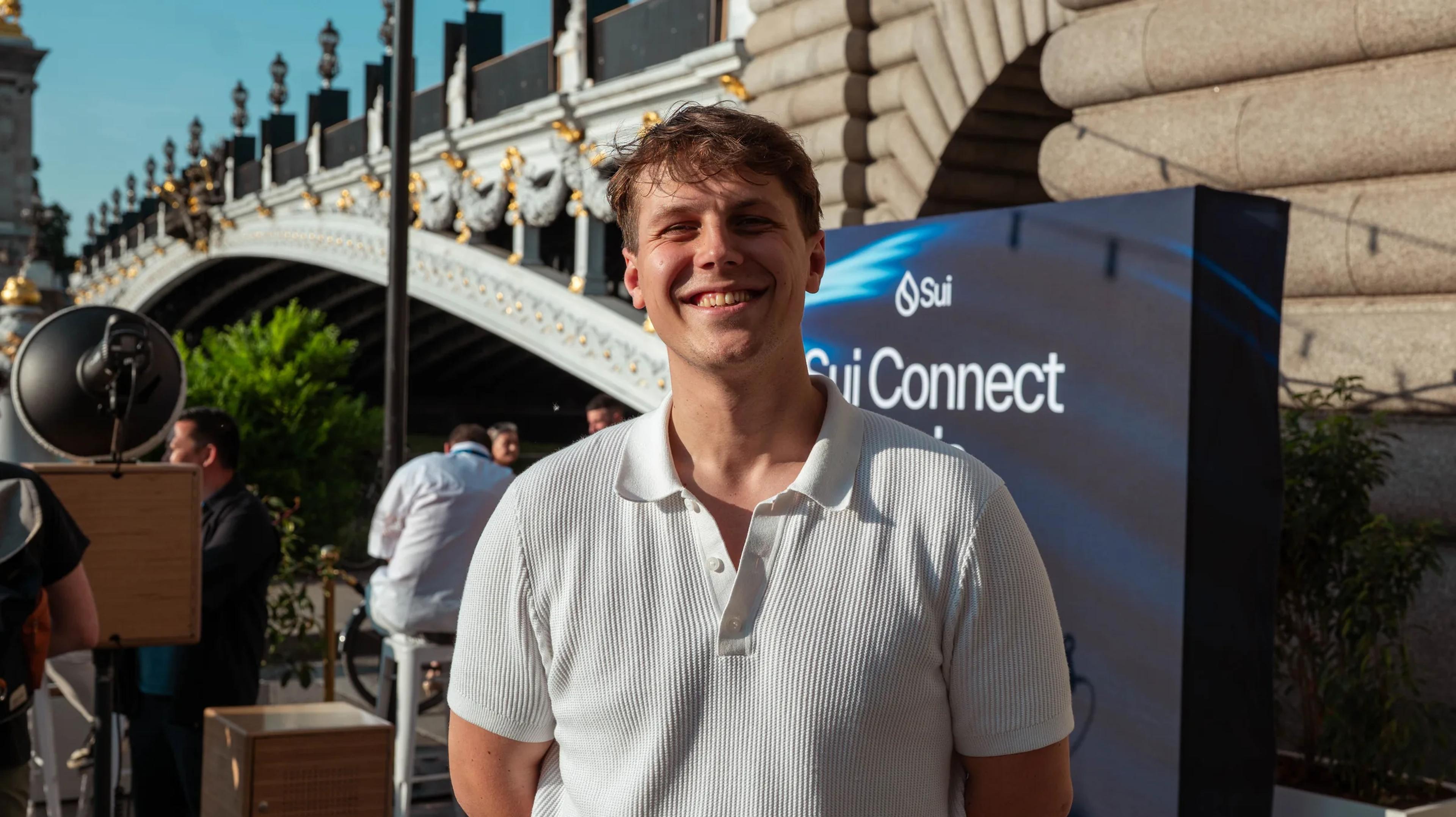 An attendee smiling beside the Sui Connect sign on the Seine riverbank