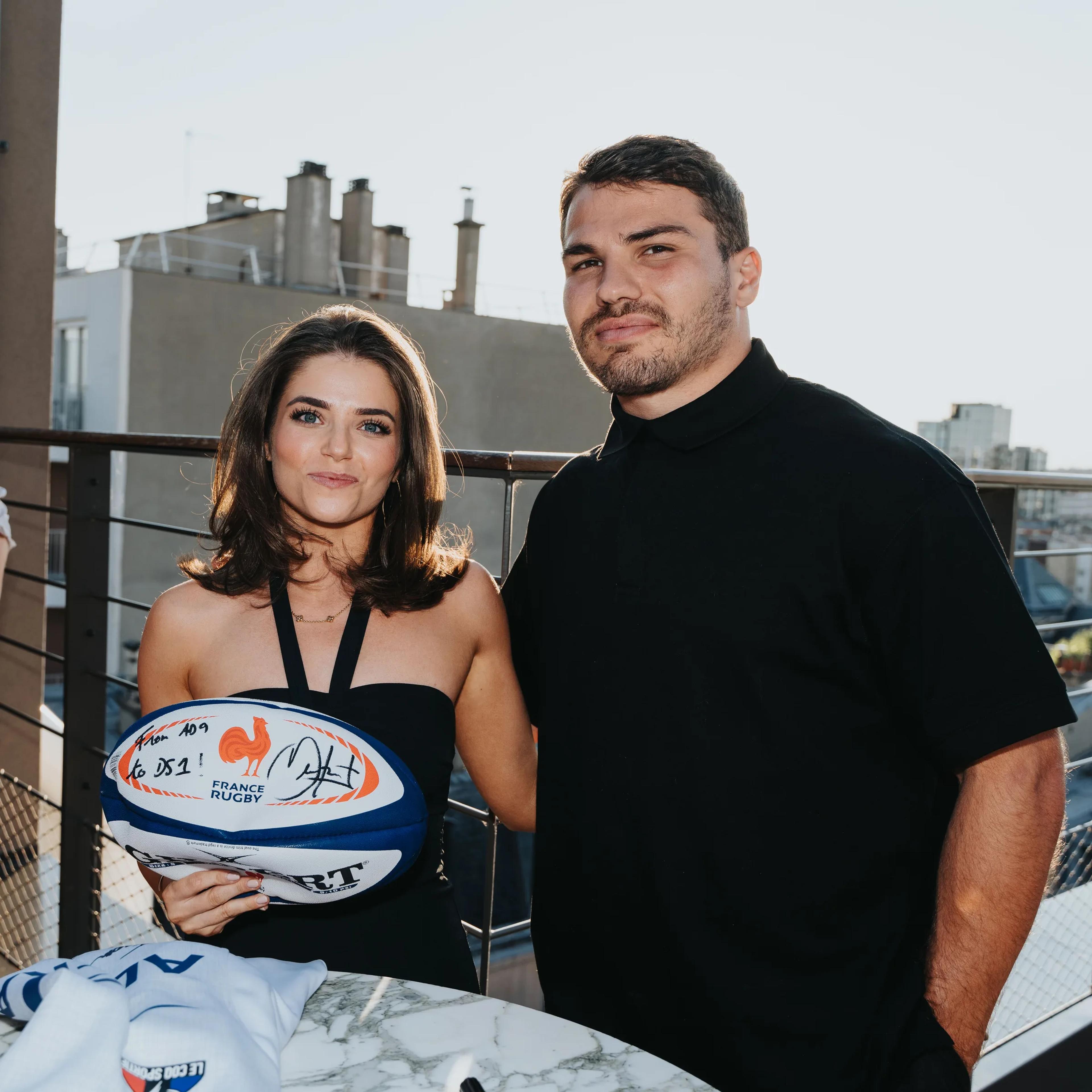 A guest and a rugby player posing with a signed ball
