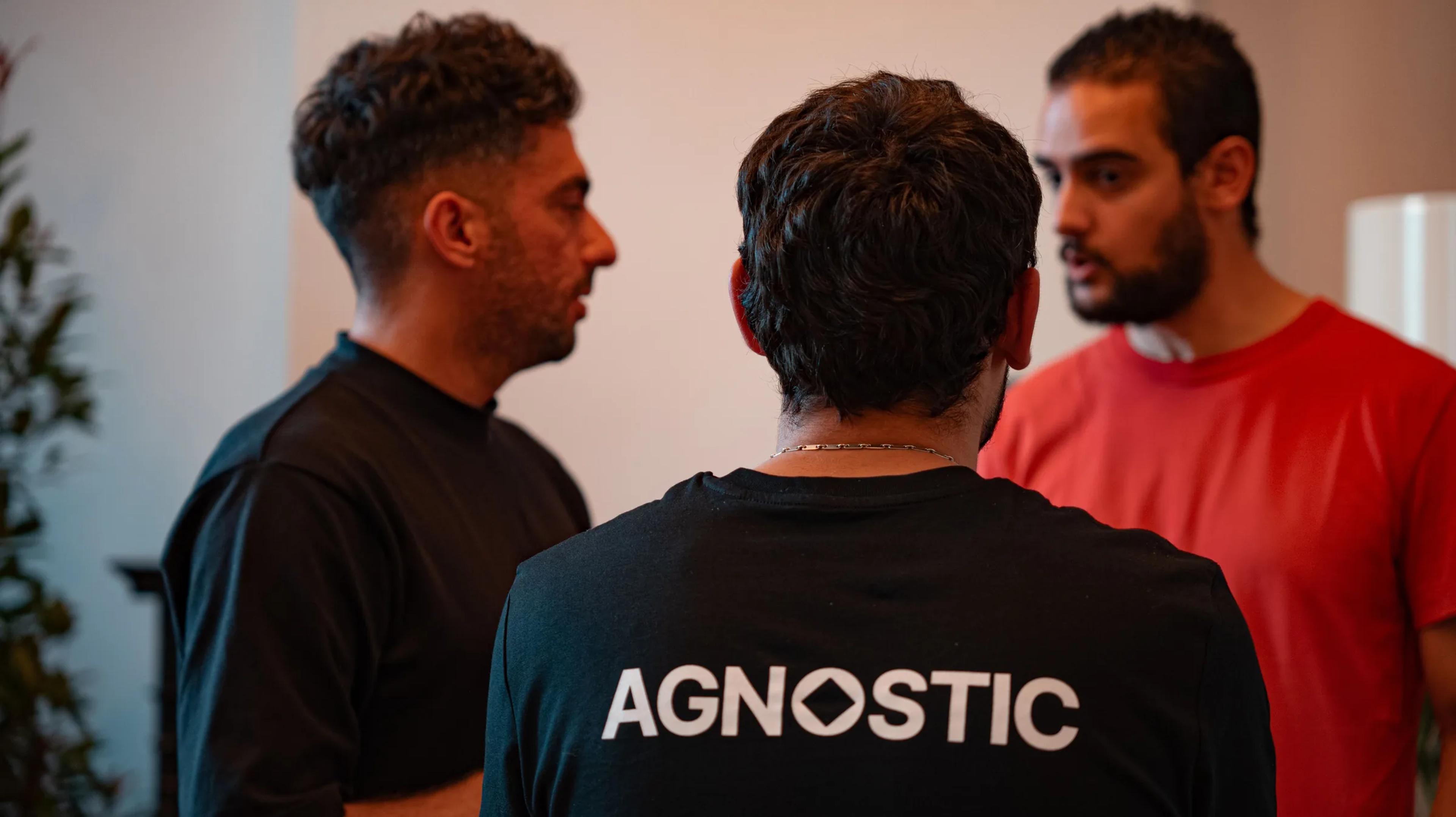 Team members in conversation, one wearing an Agnostic T-shirt