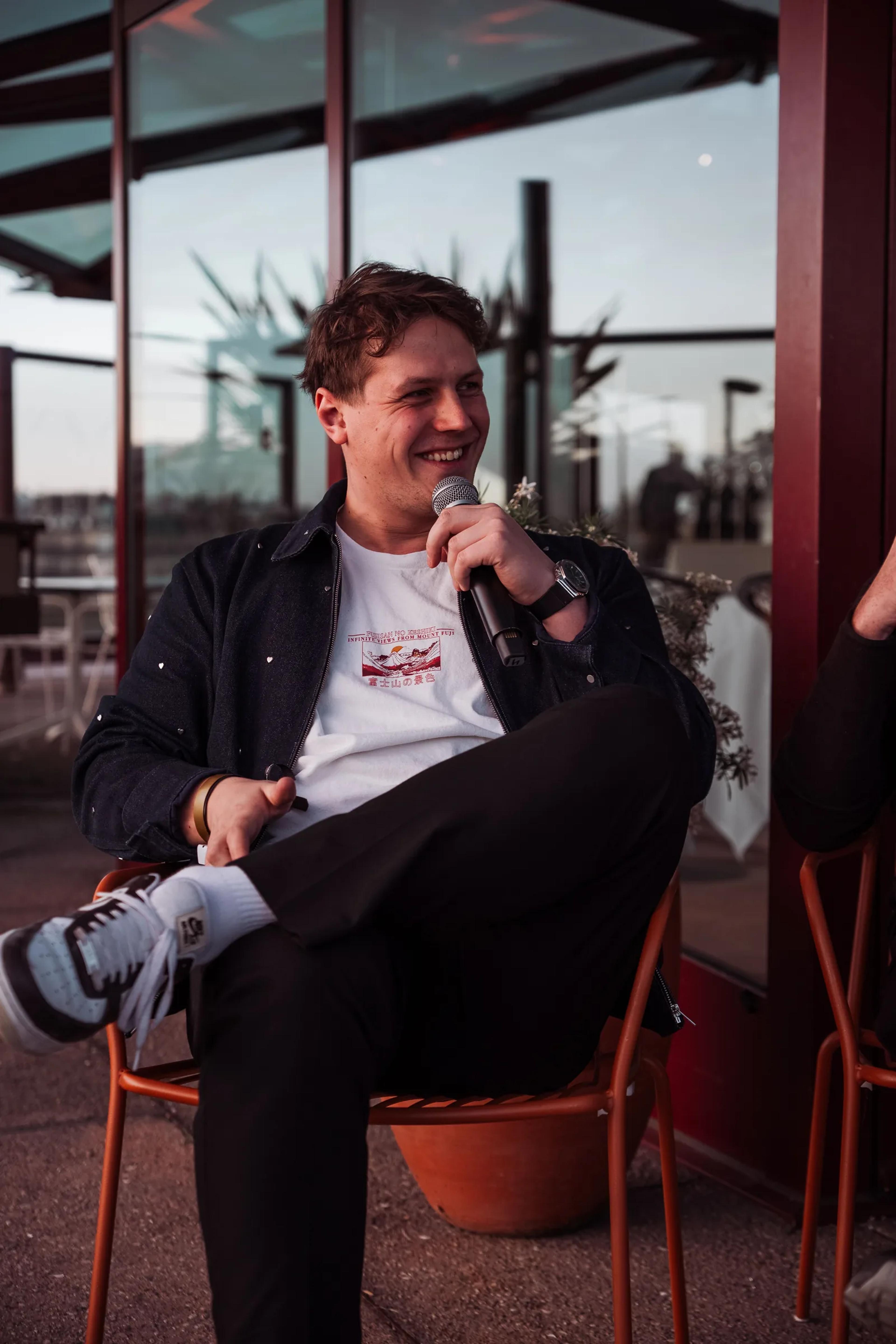 A speaker with a microphone during a seated fireside chat on the rooftop