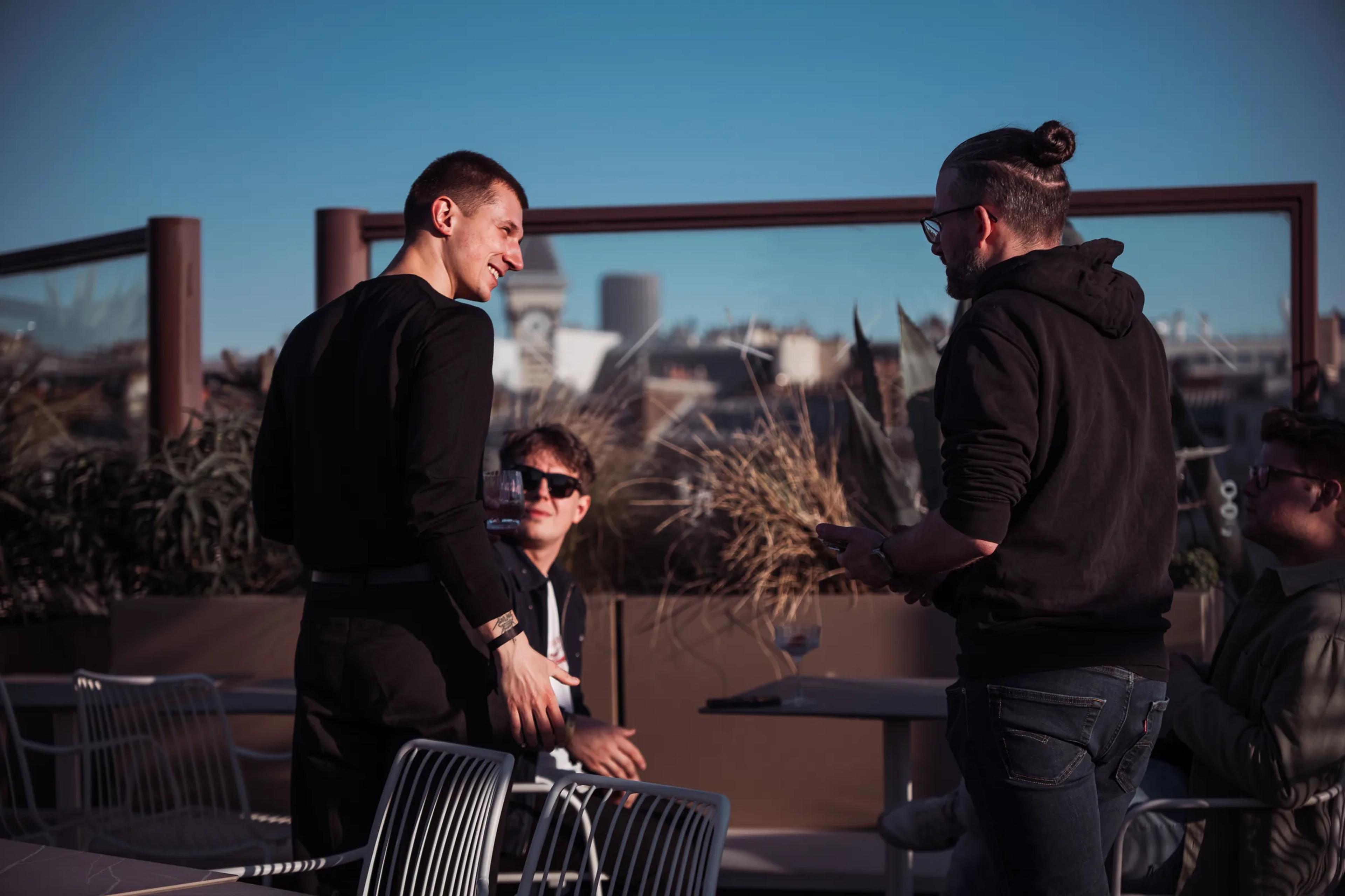 Guests talking by the rooftop railing in the afternoon sun