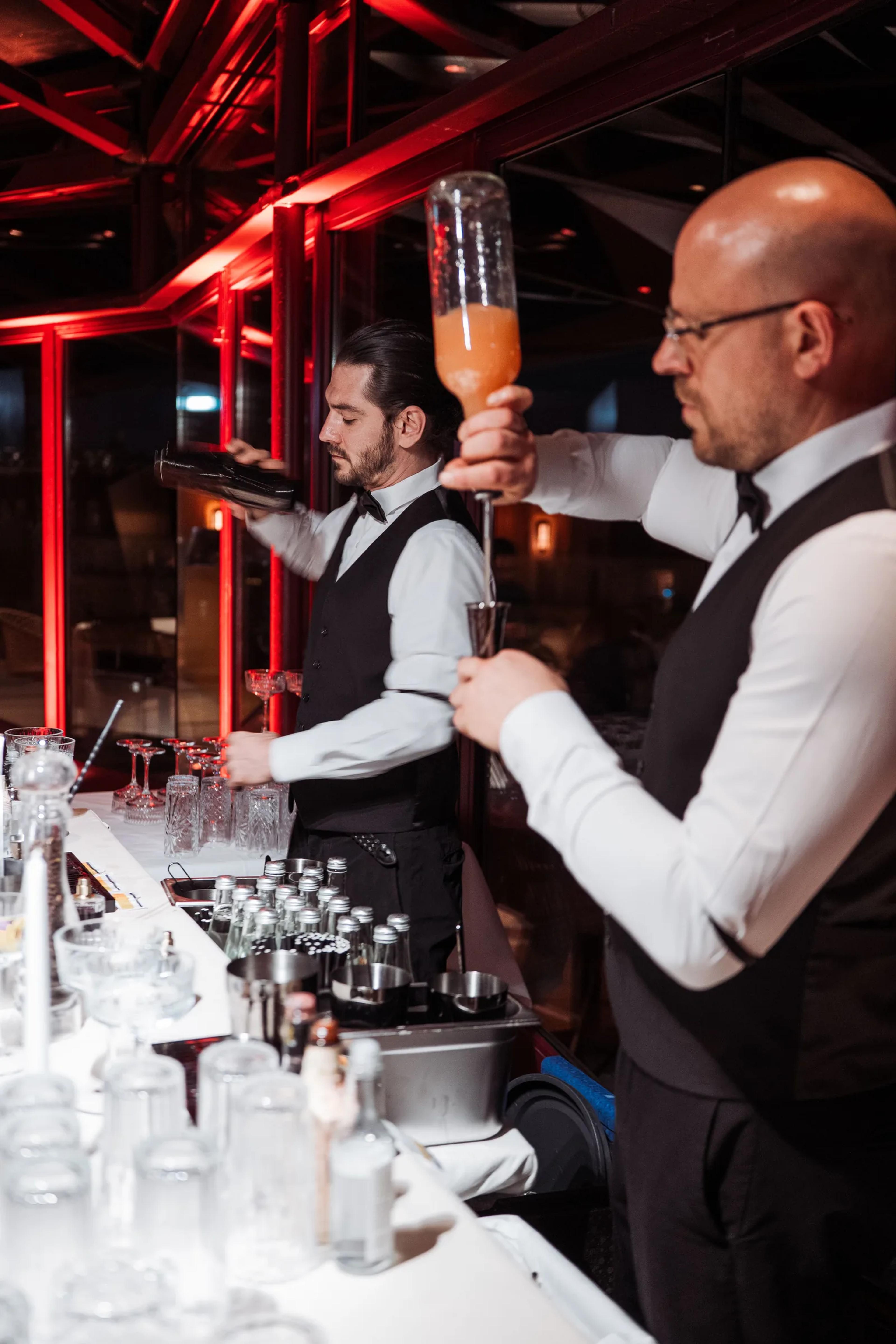 Bartenders pouring cocktails under red lights at the dYdX event