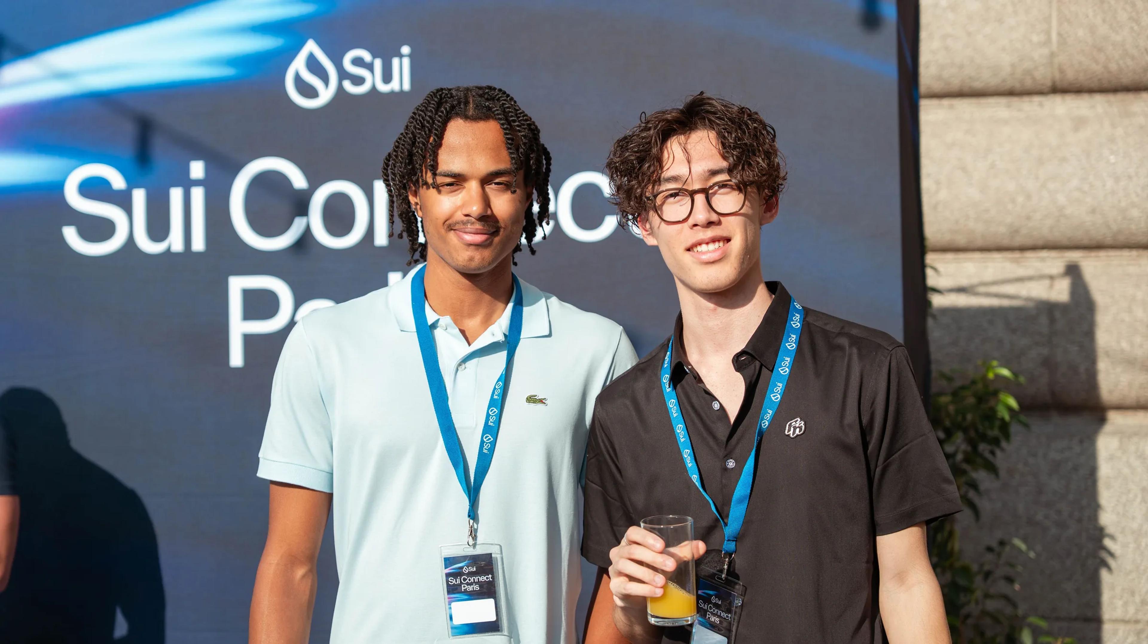 Two attendees in front of the Sui Connect Paris backdrop