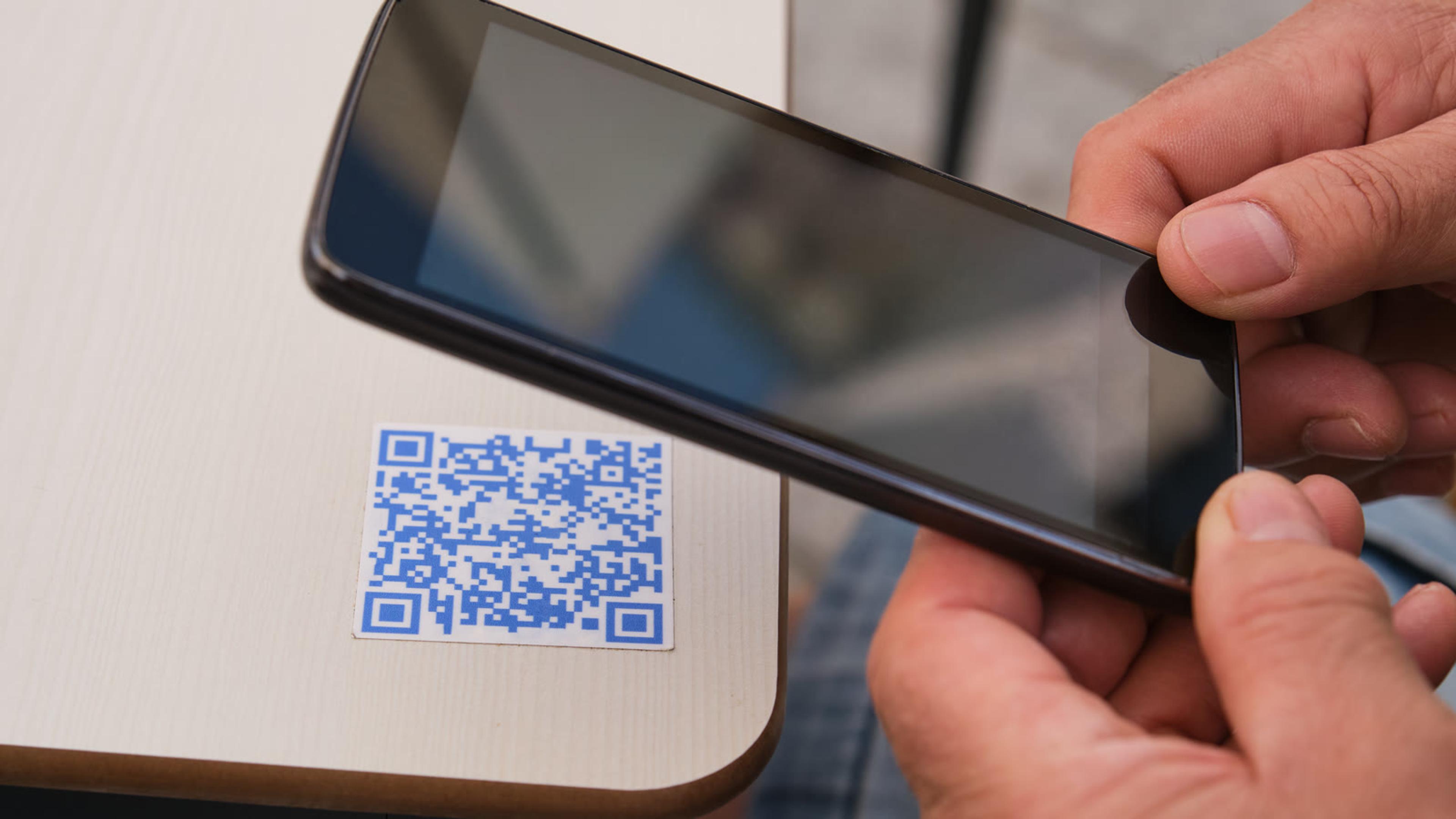 Hands holding a smartphone over a QR code, the way a new team member sets up the mobile phone app