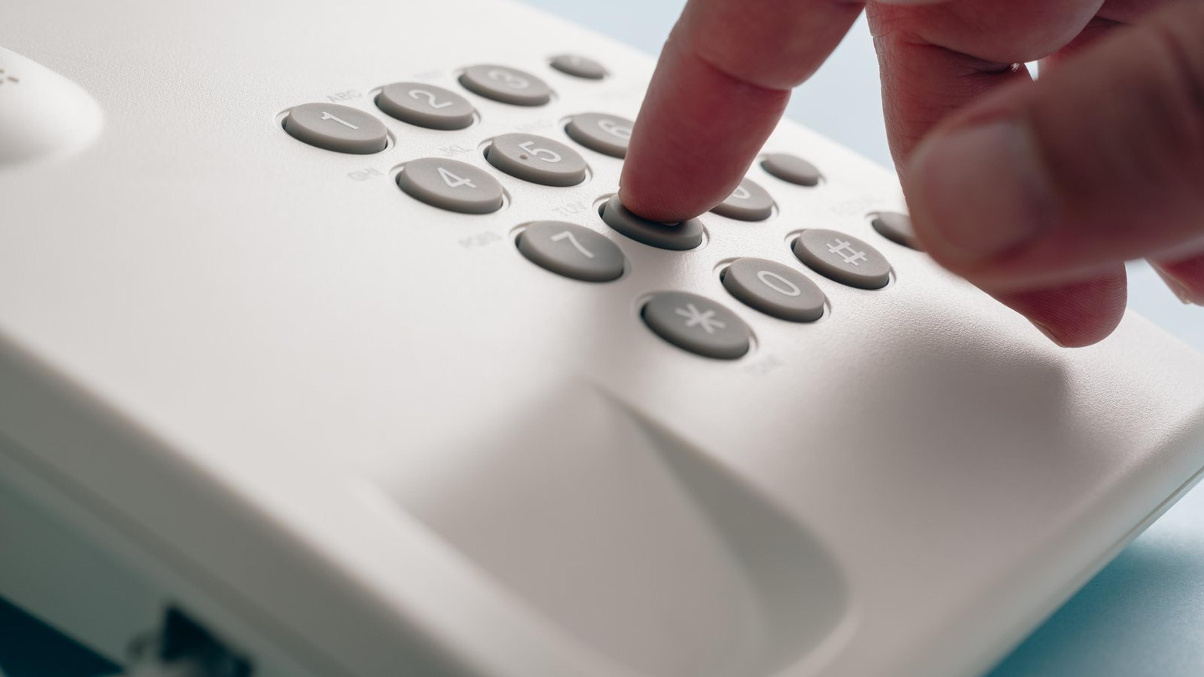 Close-up of a finger pressing the keypad buttons on a white corded office phone