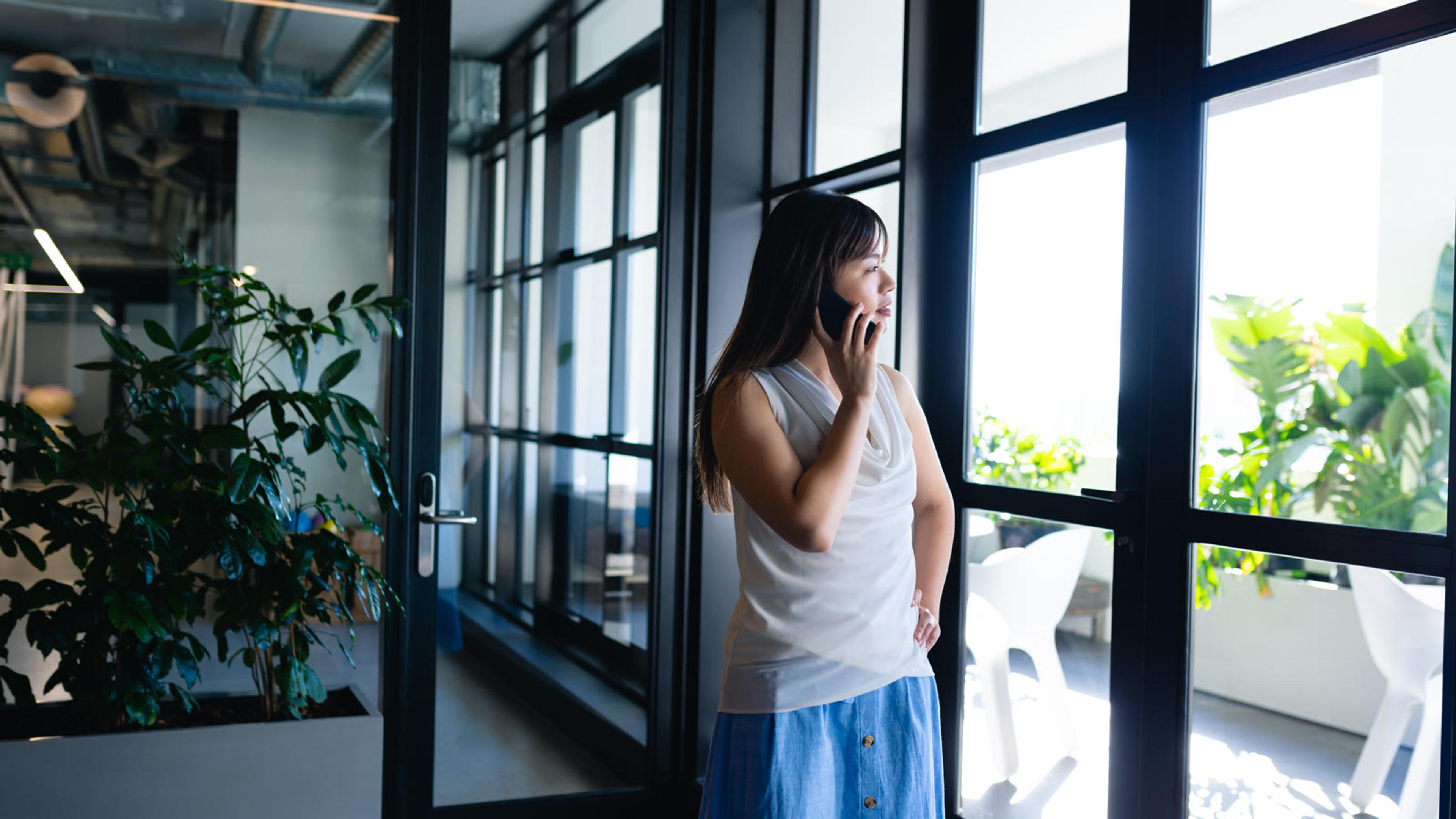 Woman talking on a cellphone in a modern office — branded mobile softphone app for resellers