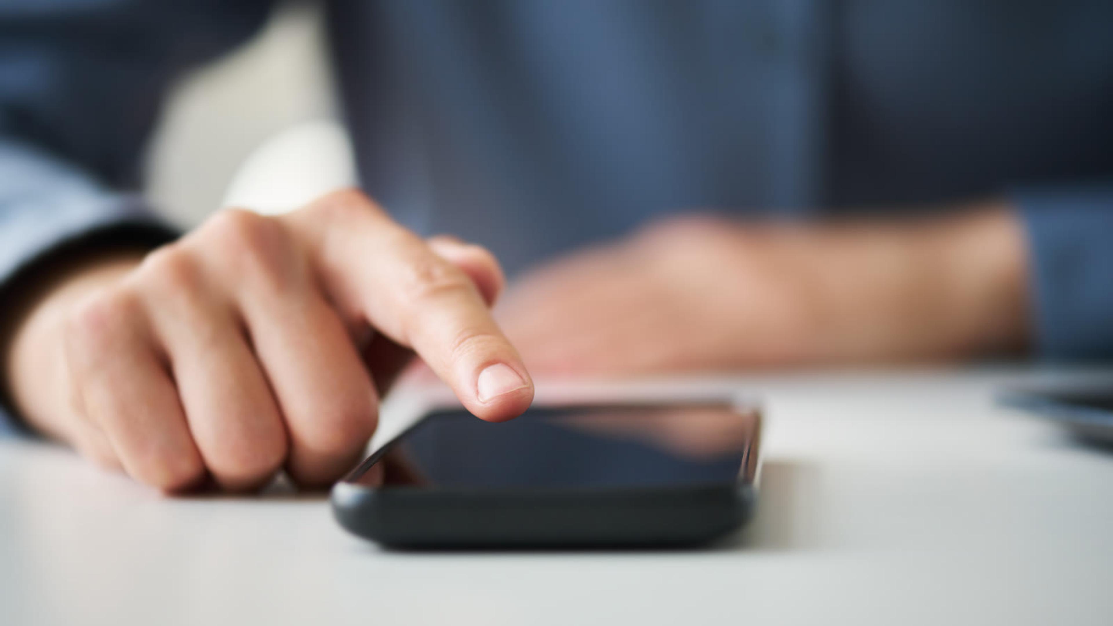 Hand using a smartphone on a white office desk