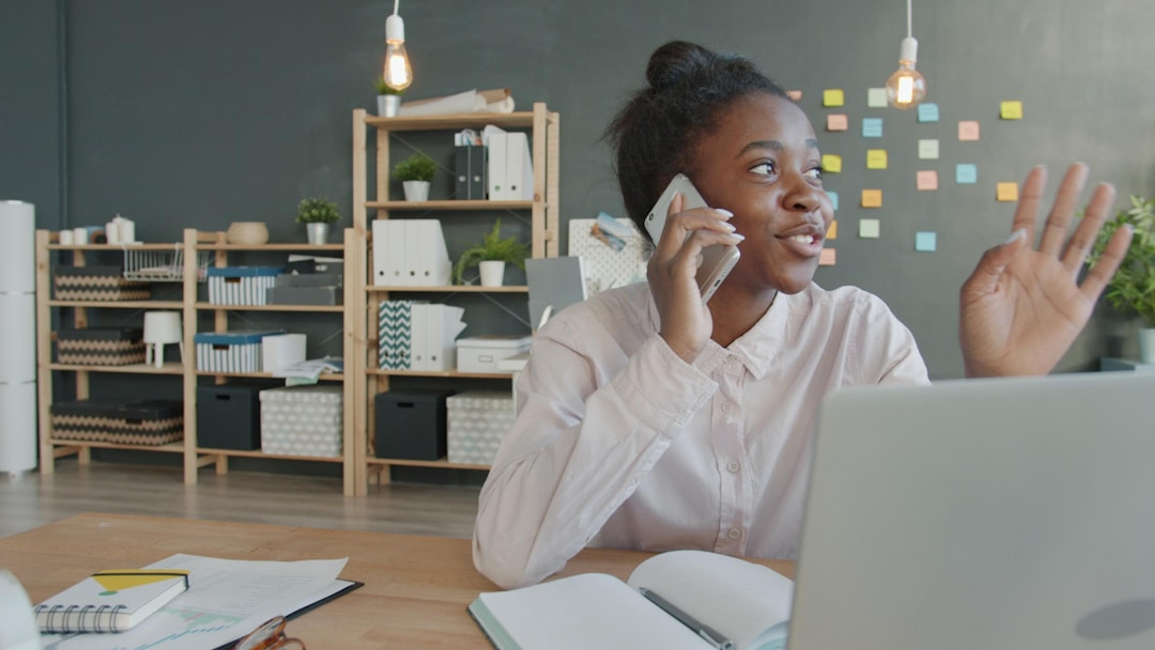 Young professional woman talking on phone at office desk with laptop open