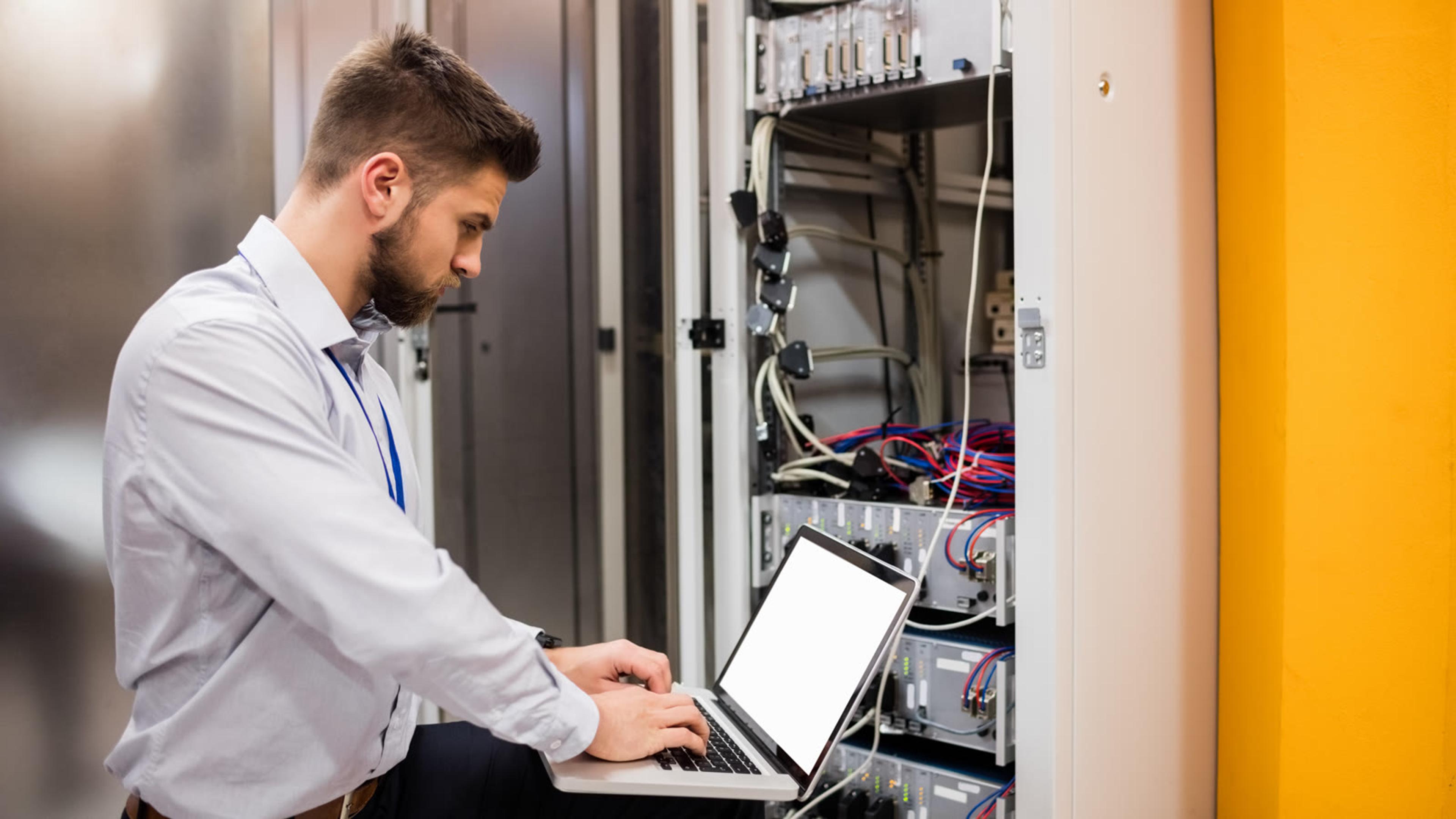 IT professional troubleshooting a server rack with a laptop in a data centre