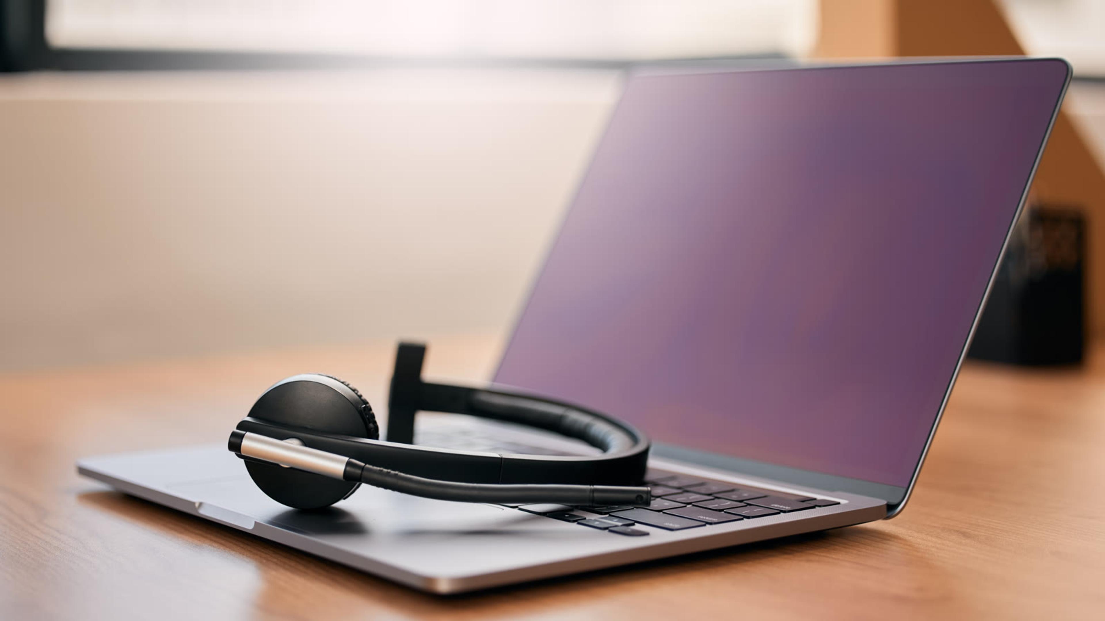 Headset resting on a laptop keyboard on a wooden desk, ready for desktop calling