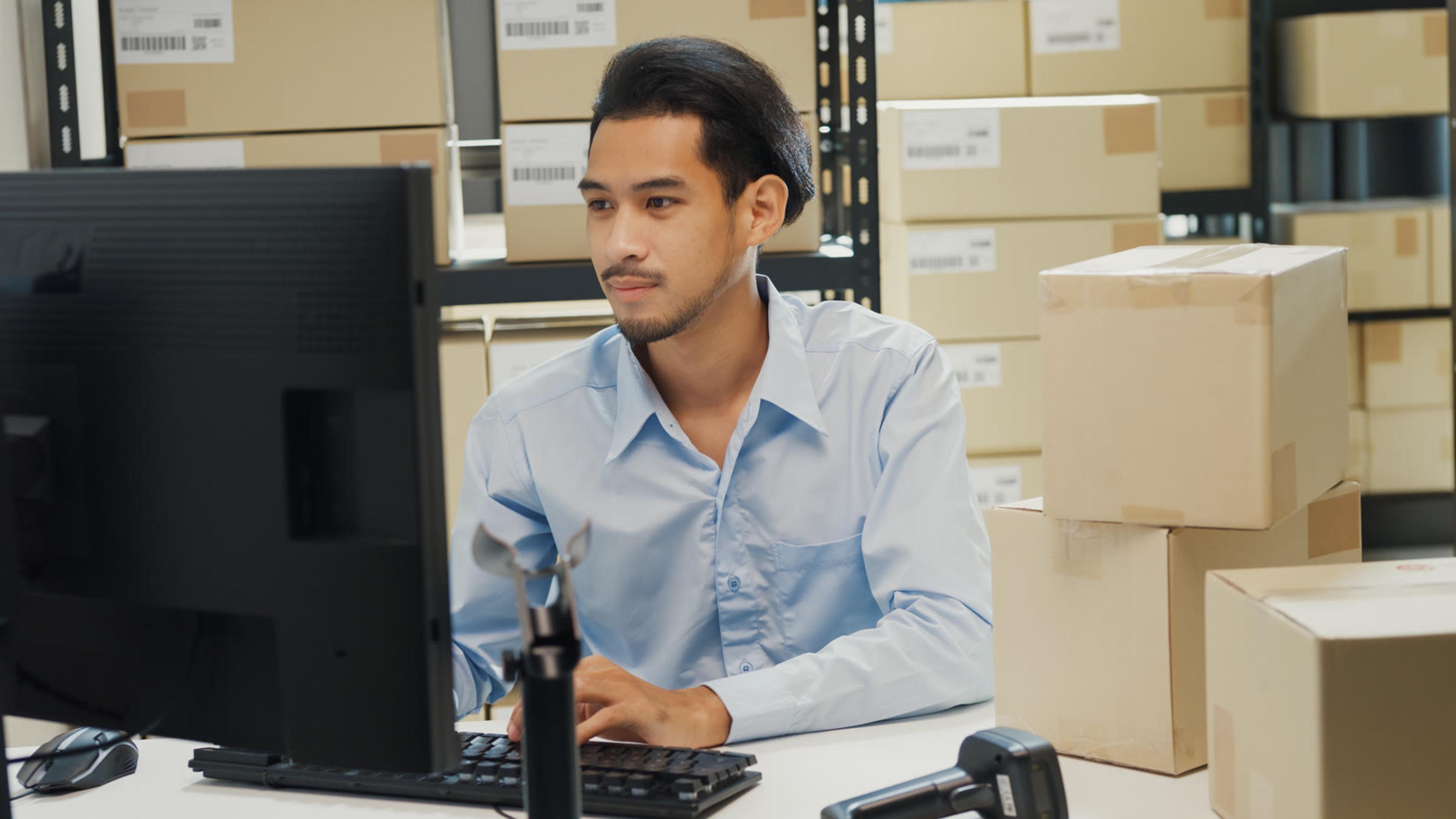 Logistics coordinator working at a computer among warehouse shipping boxes