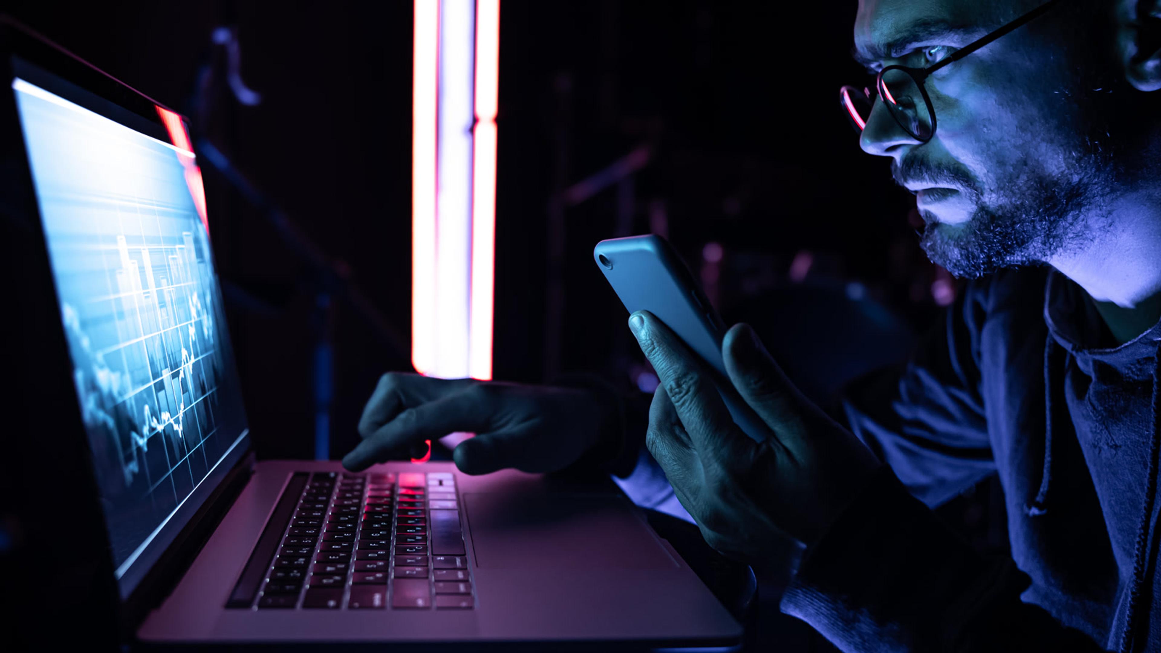 Man working on laptop with phone in a dark room — SIP TLS and SRTP for softphones