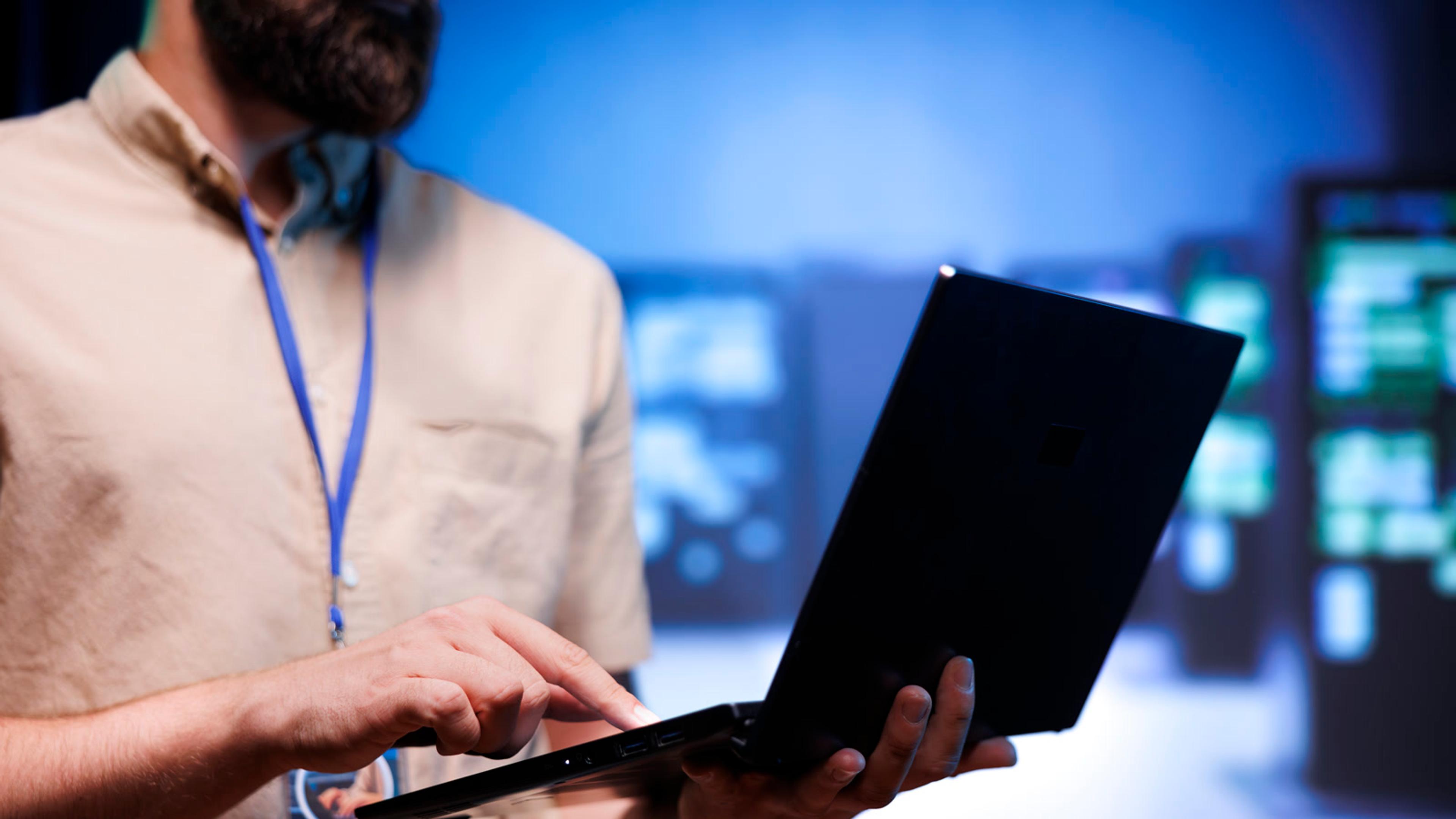 IT technician with laptop performing maintenance in a server room — testing updates before company-wide rollout