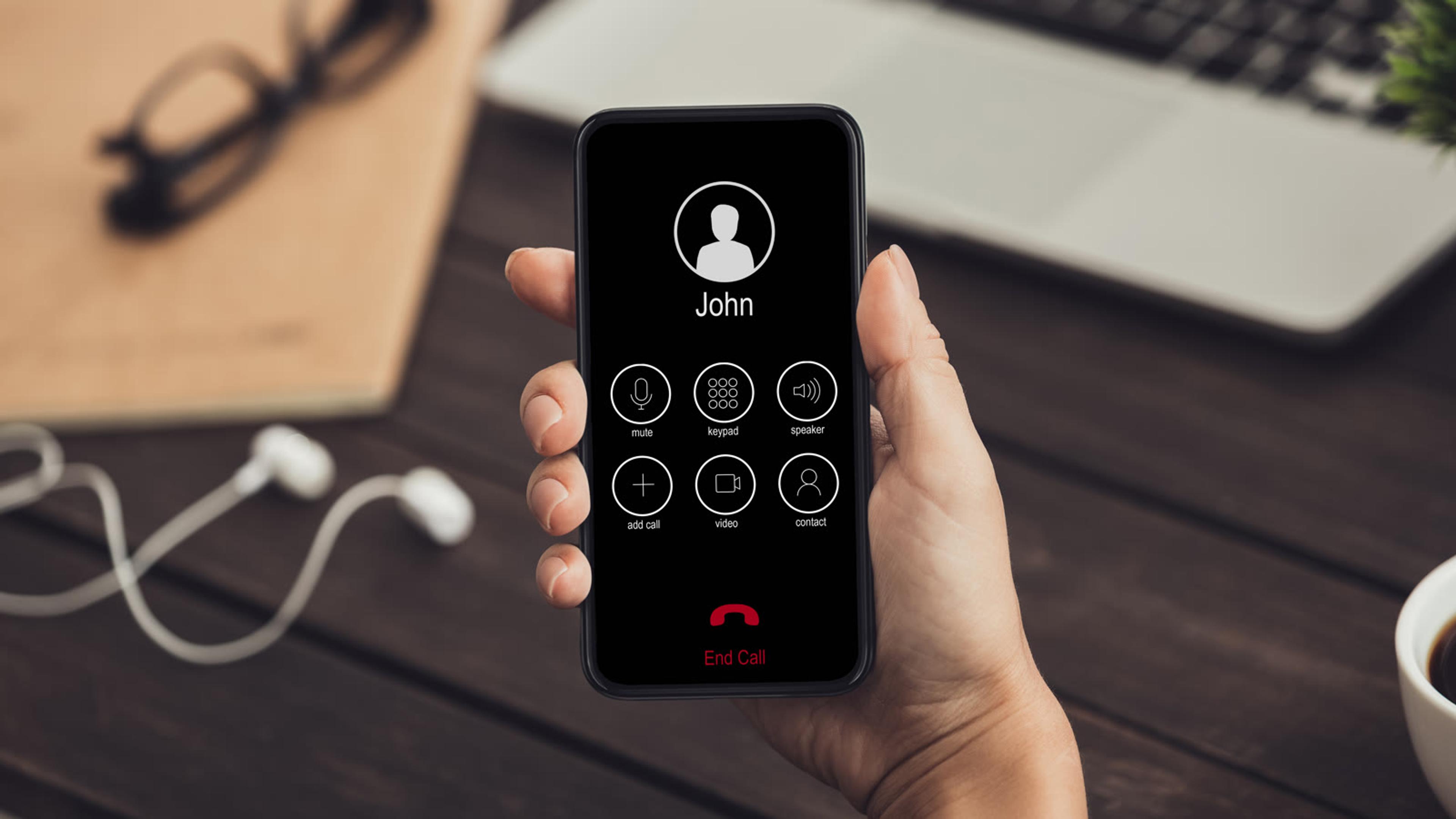 Person holding a smartphone on a desk during a call
