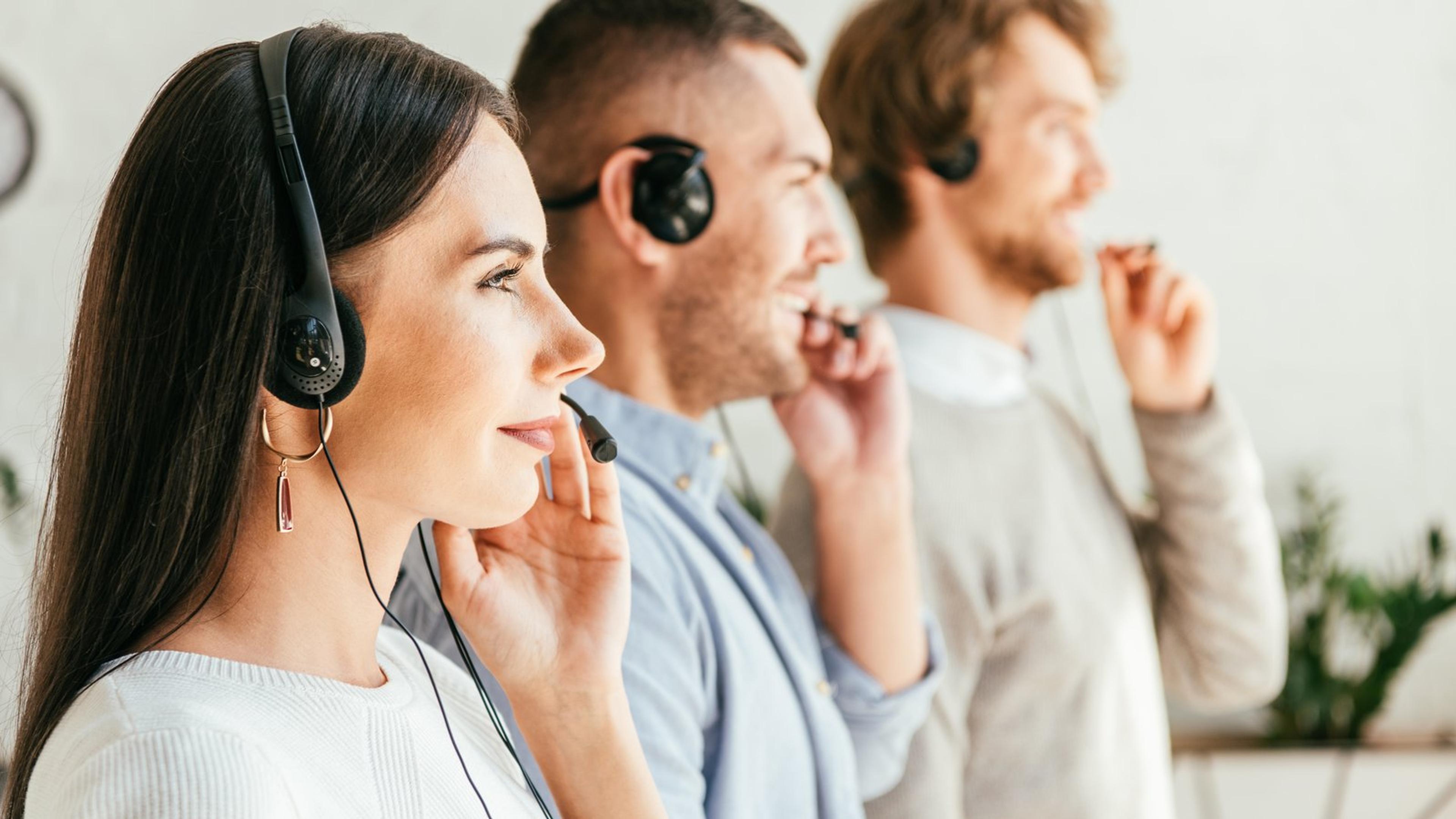 Three customer service staff wearing headsets taking calls in an office