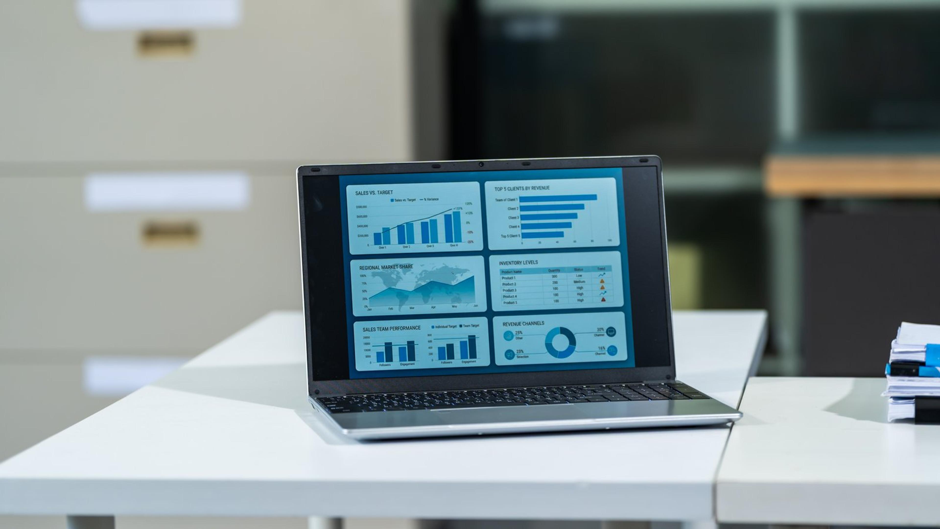Open laptop on a white office desk showing a business dashboard of bar charts and graphs