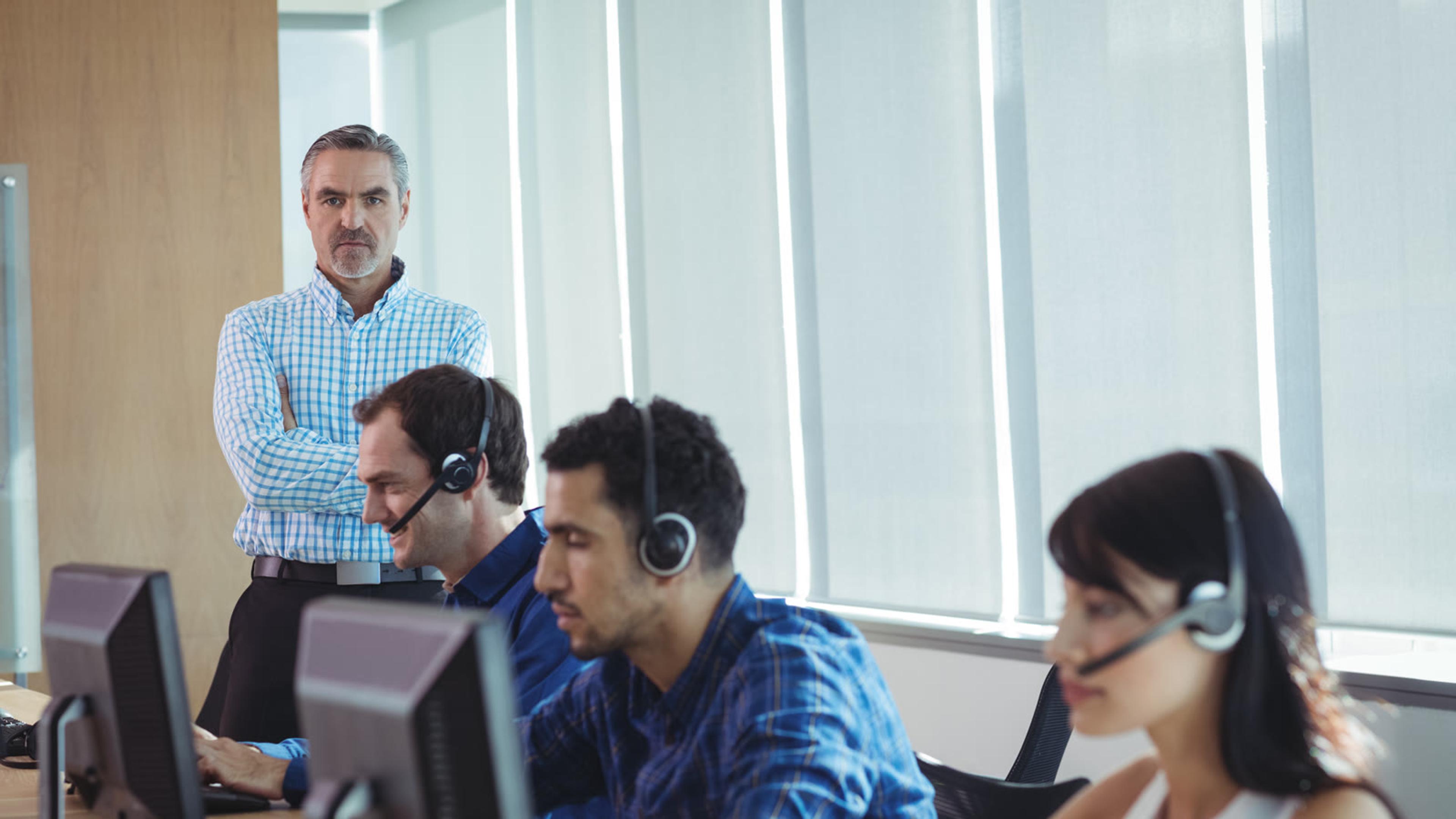 Manager supervising call agents wearing headsets at their desks