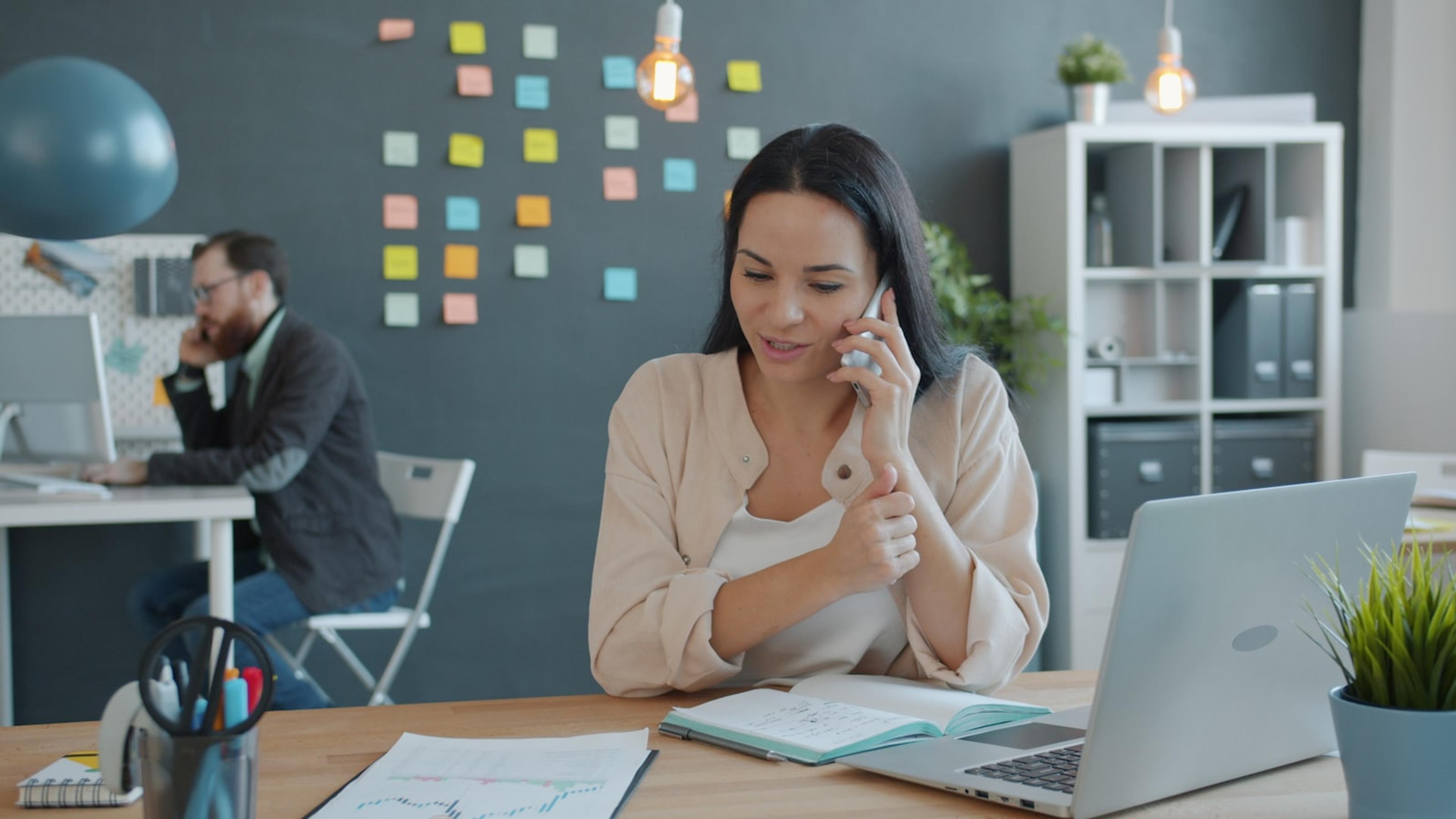 Remote business employee making a mobile call beside a laptop