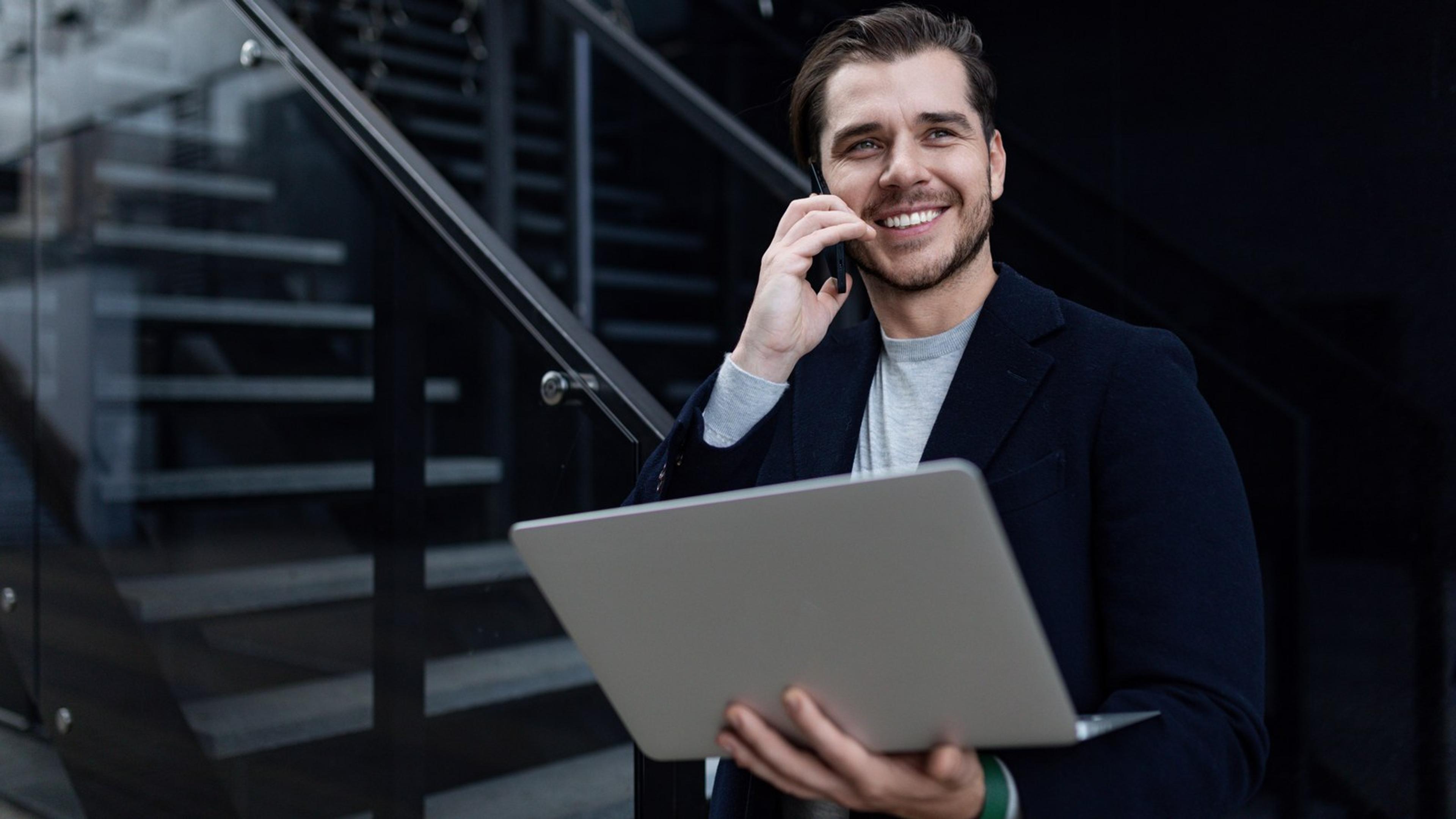 Smiling sales professional with laptop talking on phone outdoors — HubSpot VoIP mobile calling