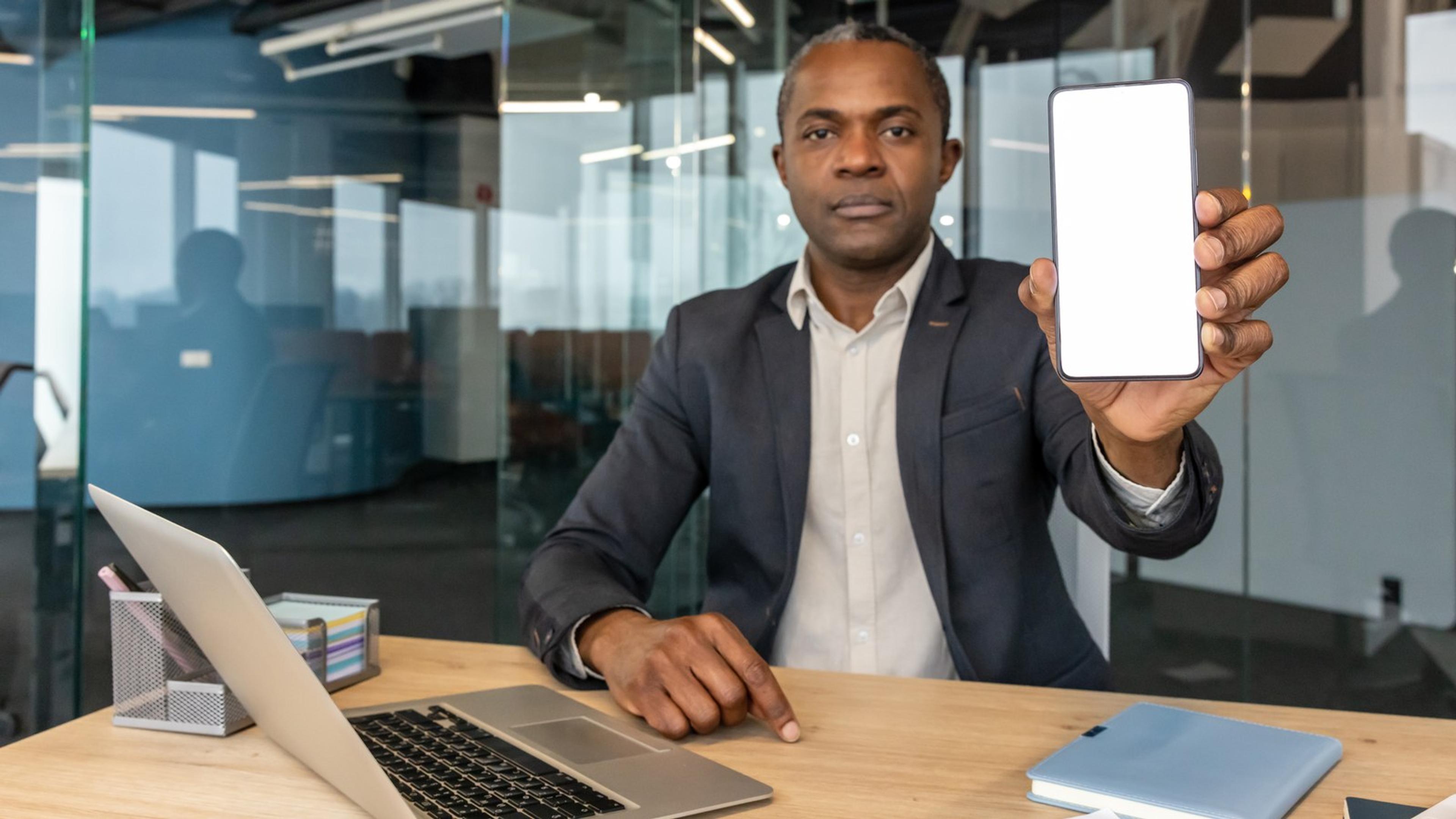 Businessman holding a smartphone at an office desk — white-label SIP softphone handset for VoIP resellers