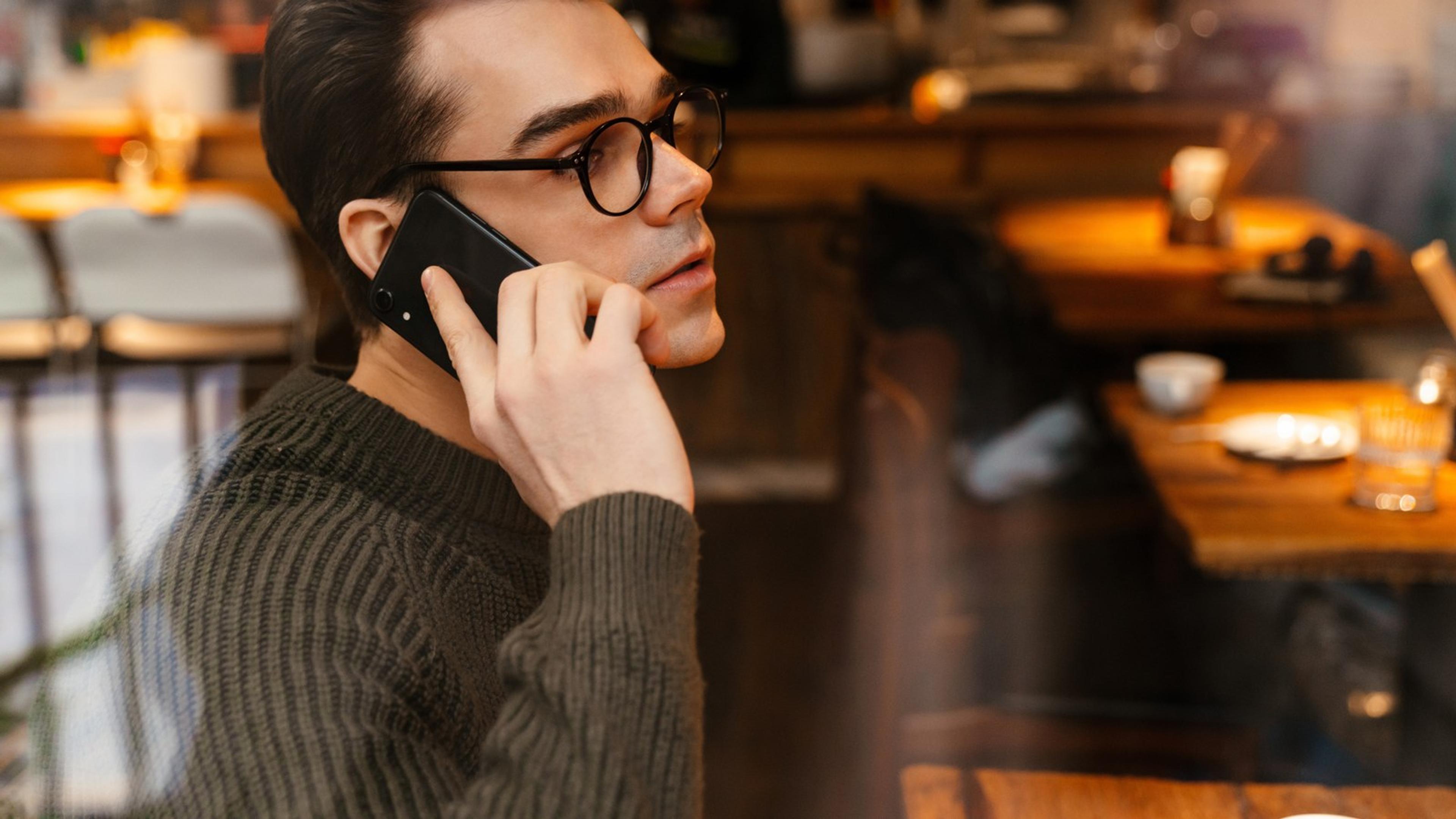 Young professional speaking on a smartphone in a cafe — mobile softphone calling for small business