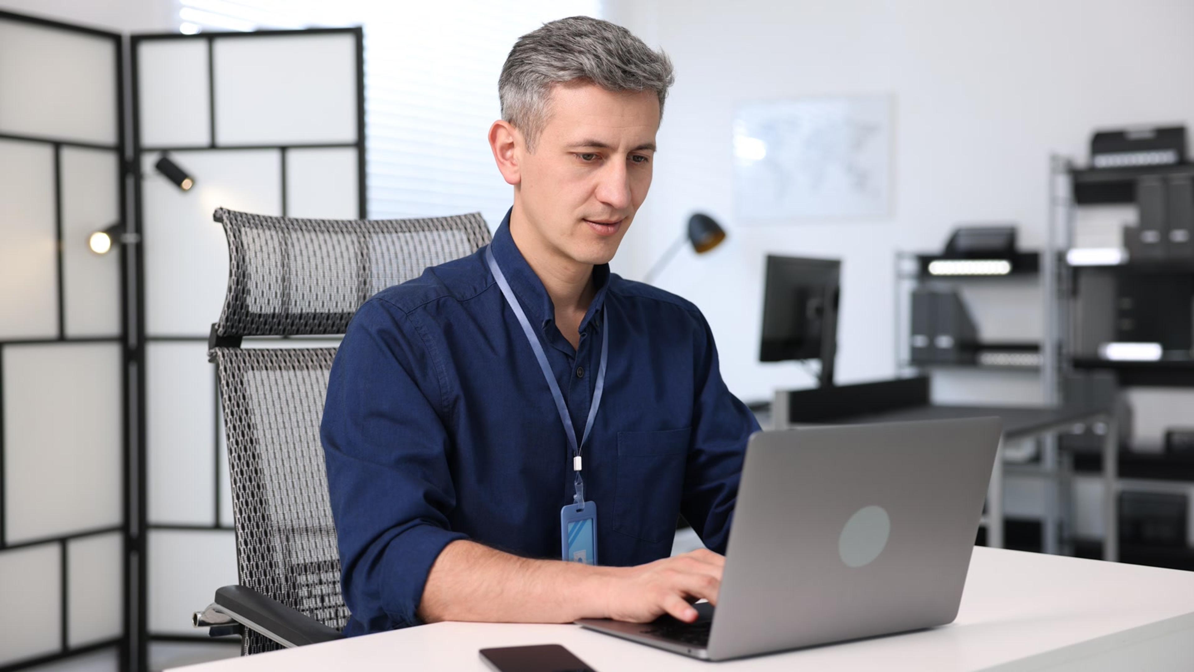 IT administrator with badge working at a laptop in a modern office — password manager rollout for SMB IT