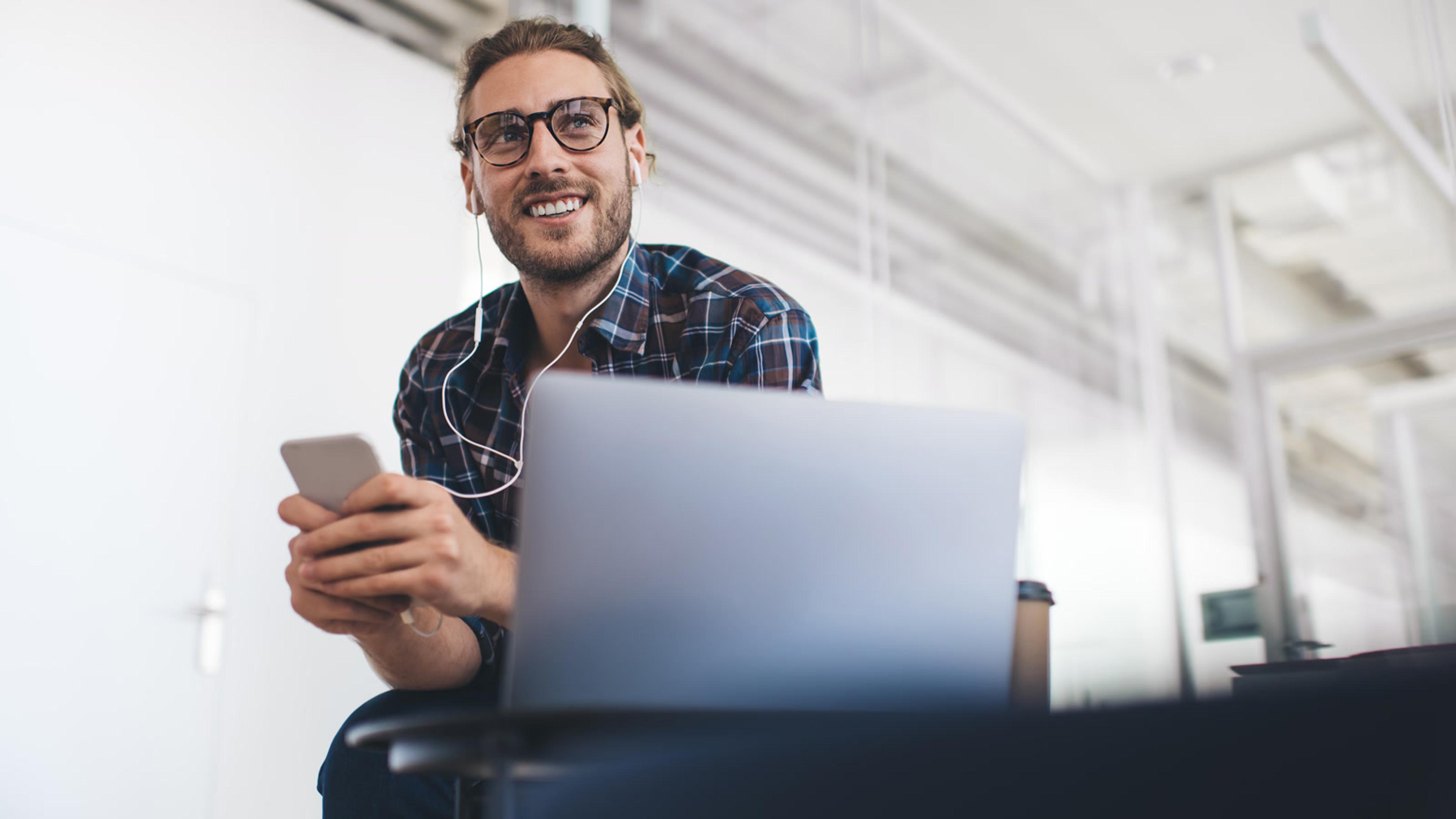 Young man using laptop and smartphone in office — mobile softphone push notifications
