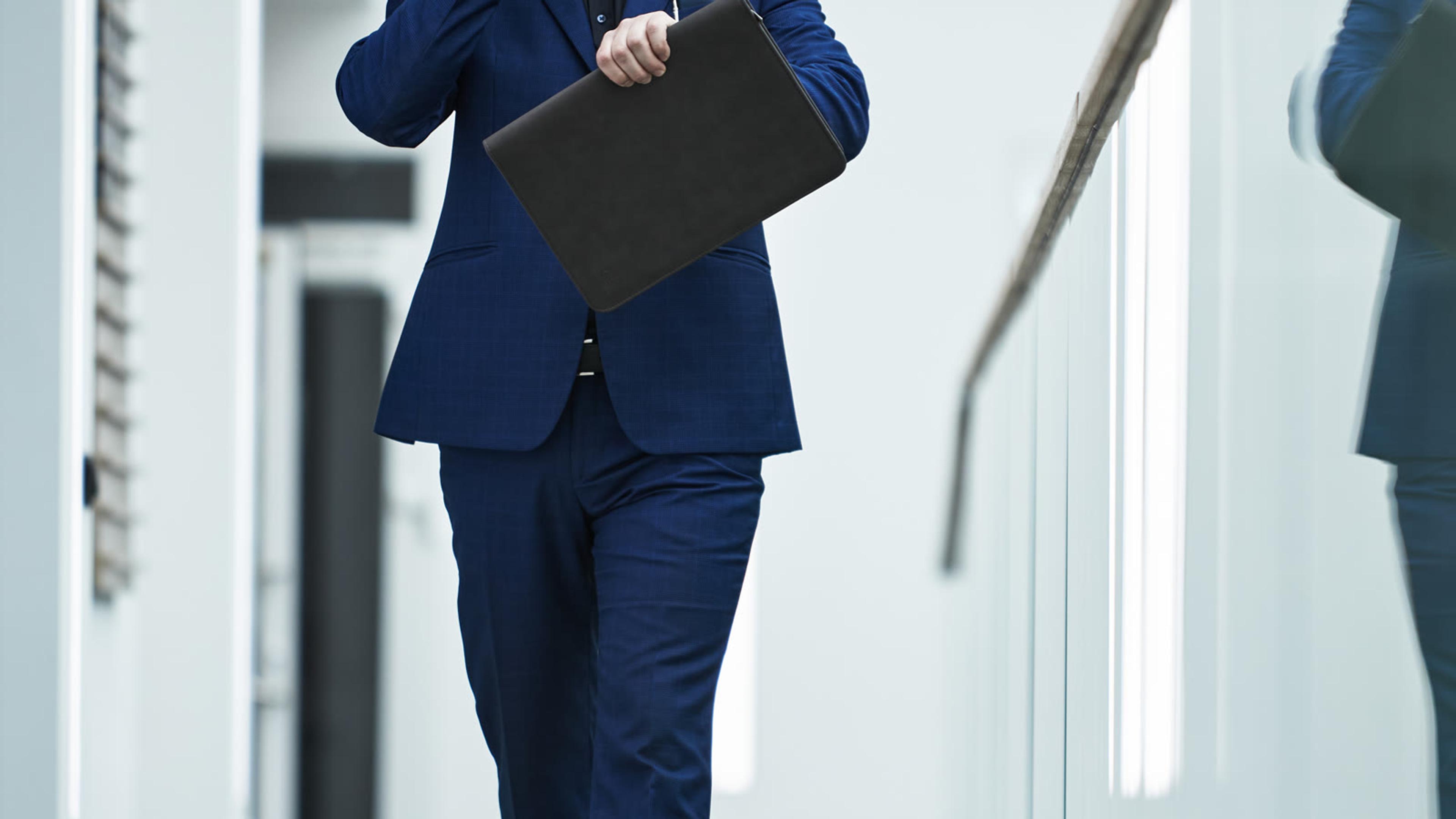 Professional on his phone walking through an office hallway, checking a colleague's status on a mobile softphone