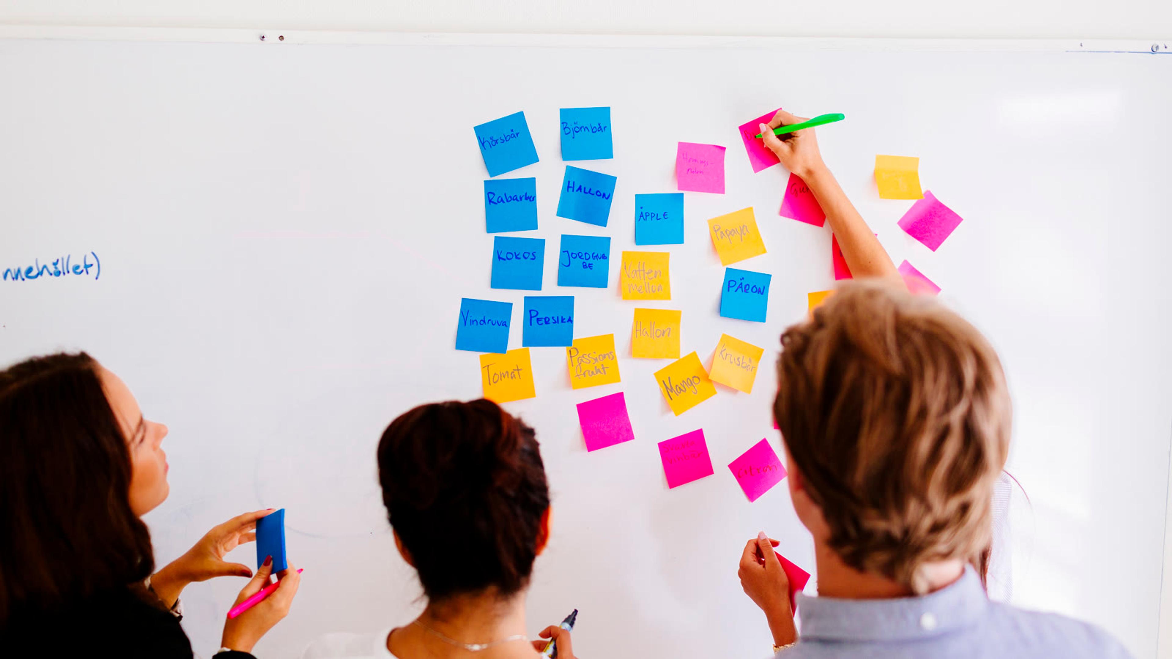 Small team arranging sticky notes on a whiteboard to map a process