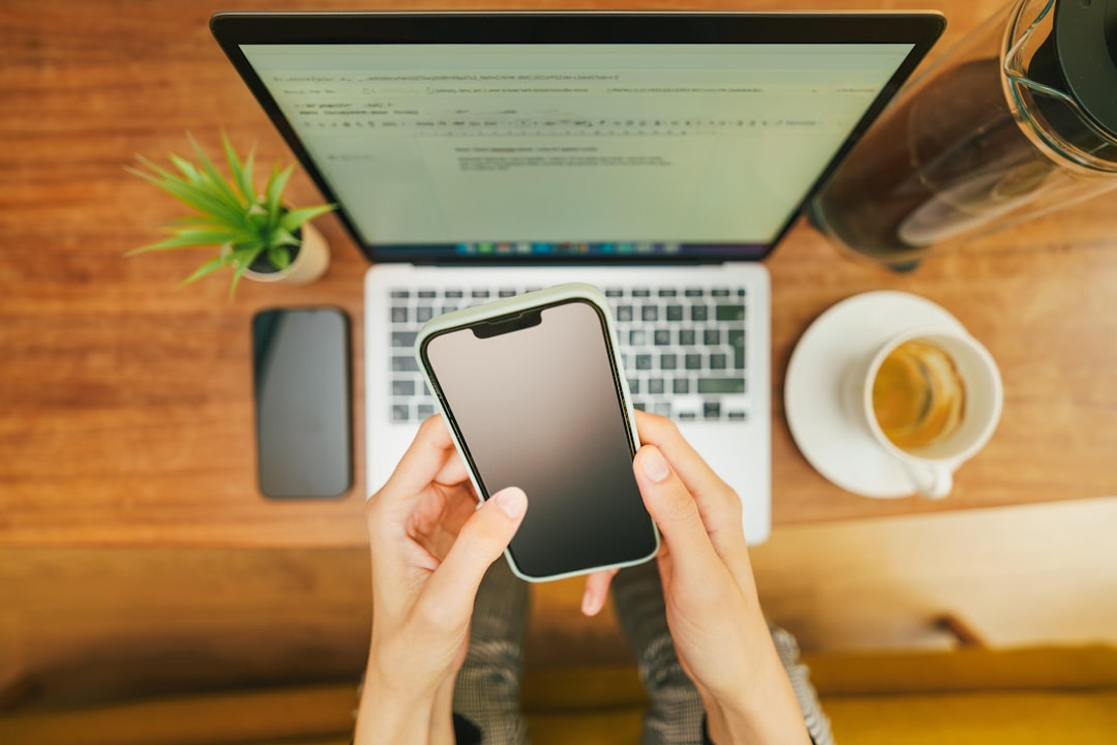 Person using a smartphone beside a laptop at a business desk