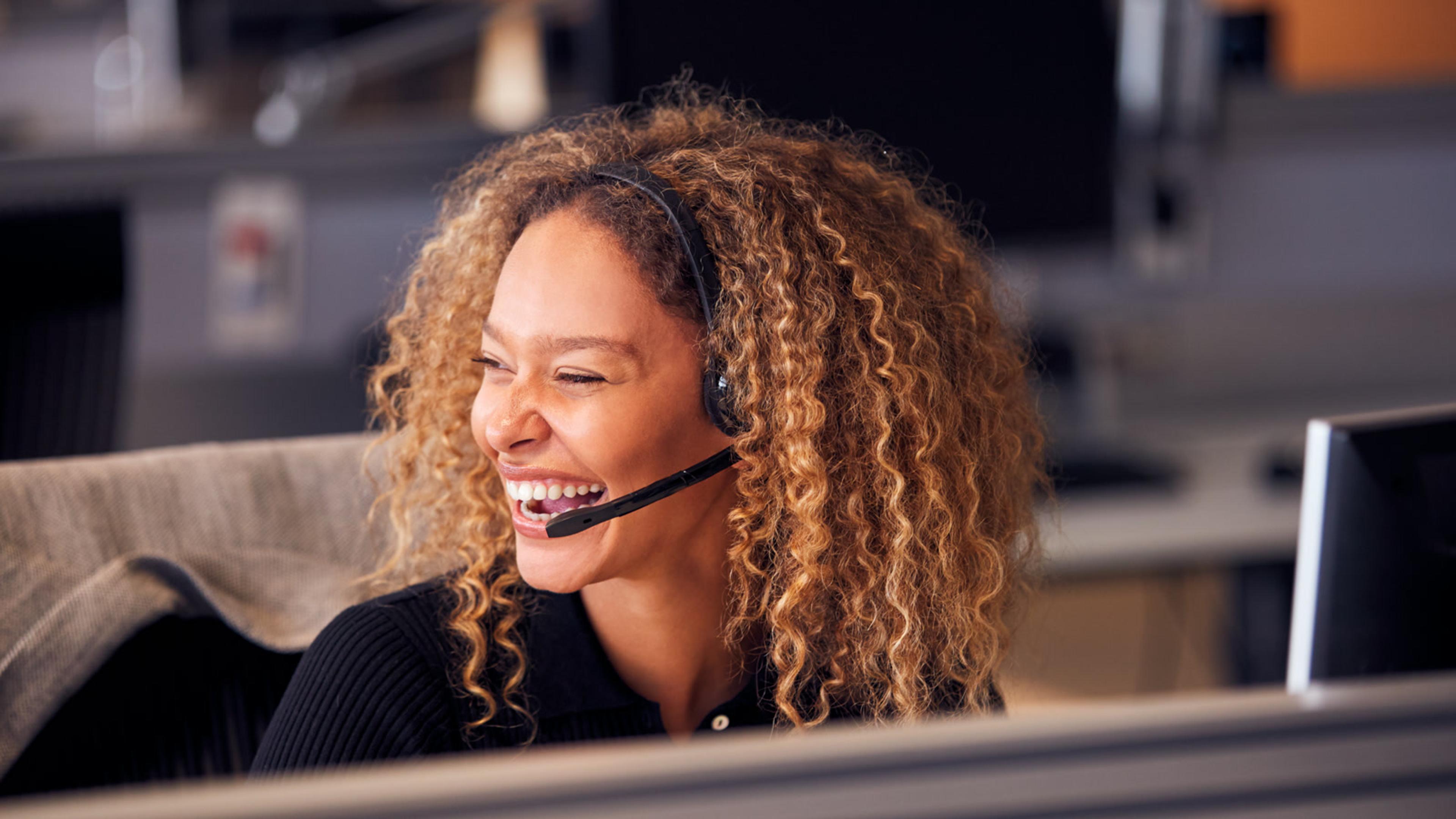 Happy woman working at a computer with a headset — white-label softphone headset lifestyle