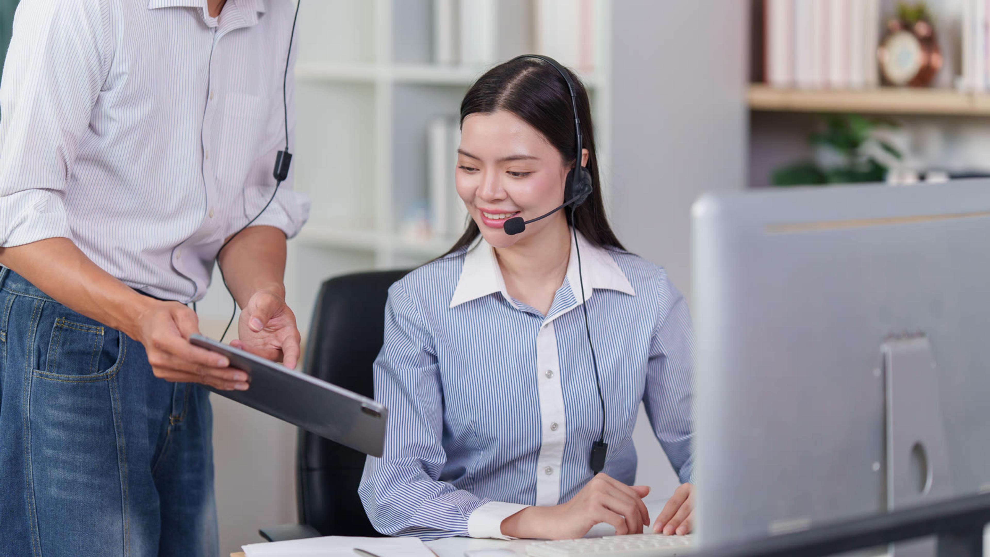 Supervisor coaching a colleague on a headset at her desktop computer