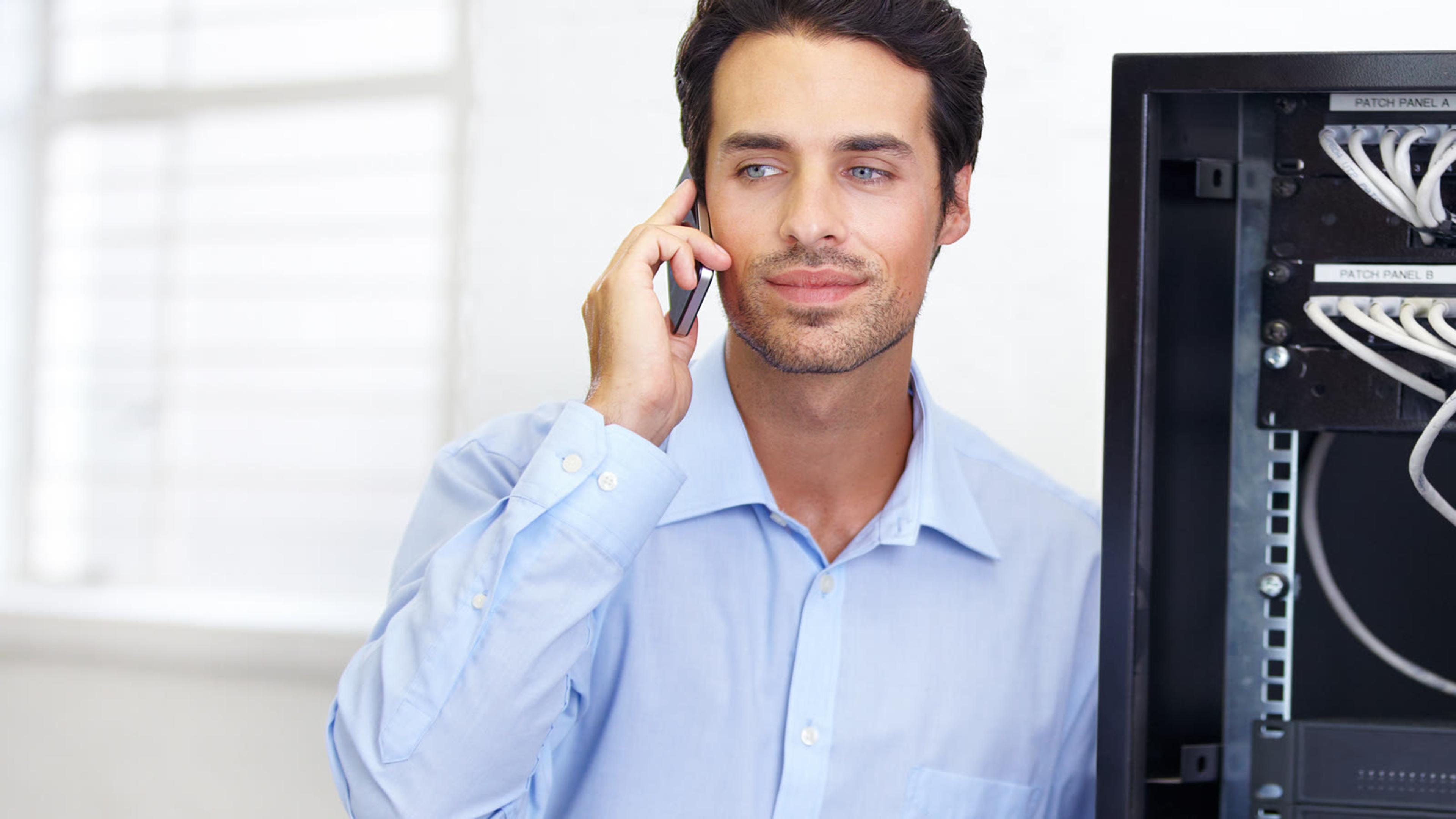 IT technician on a phone call beside a server rack, reaching a customer's phone system from his softphone