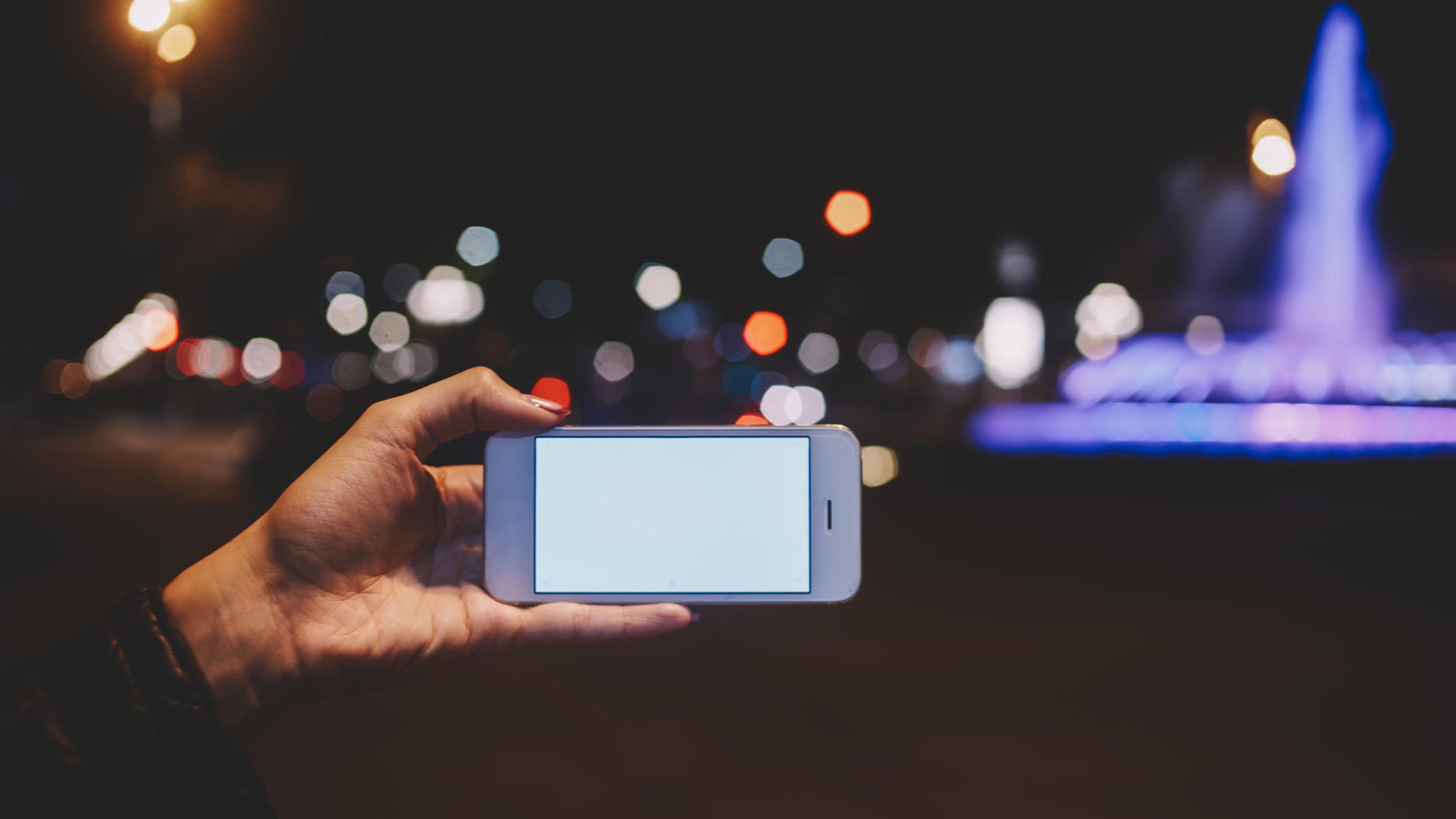 Hand holding a phone with a blank screen at night — SIP push waking a sleeping mobile