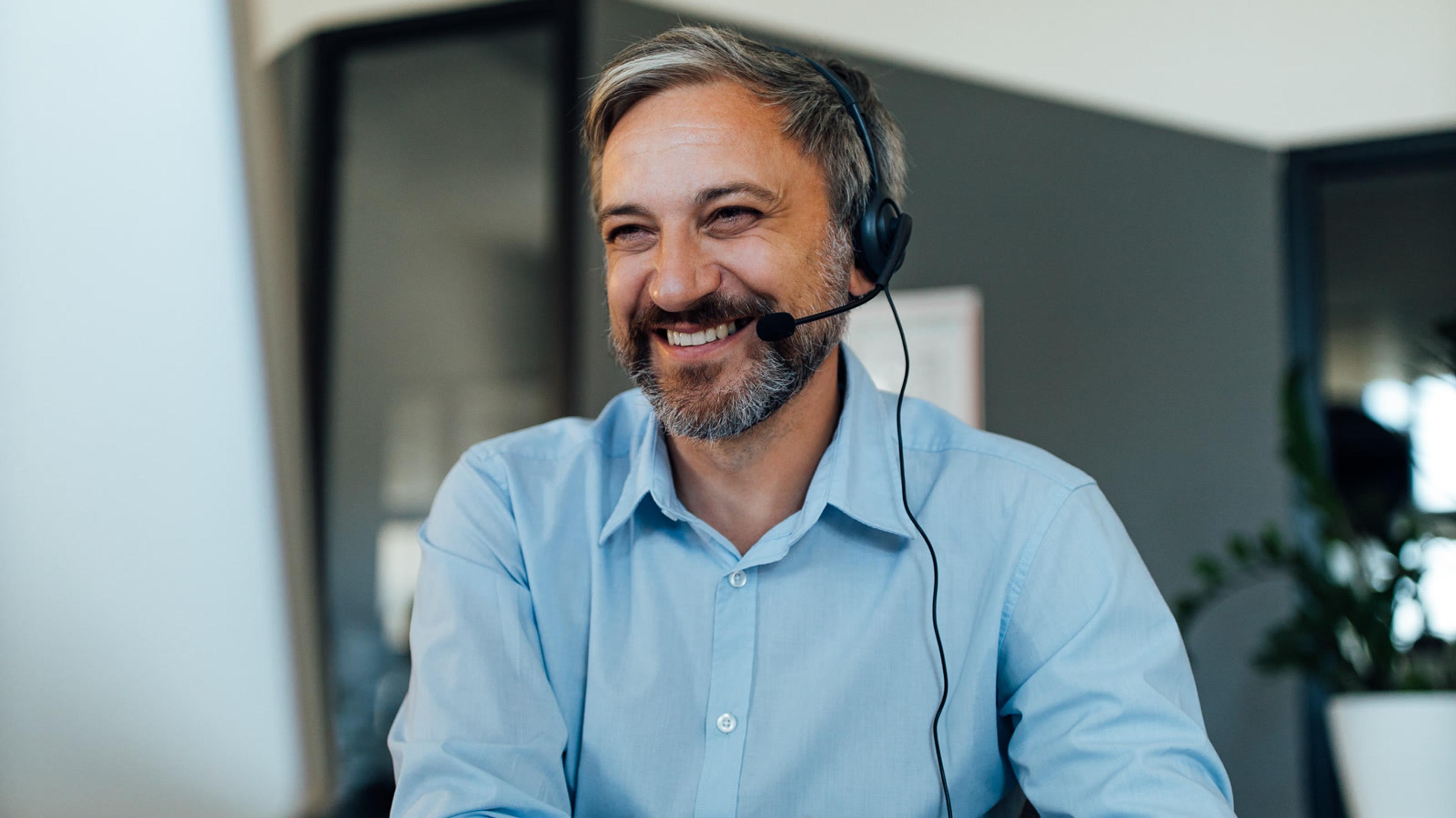 Smiling man with a headset working at a computer on a softphone