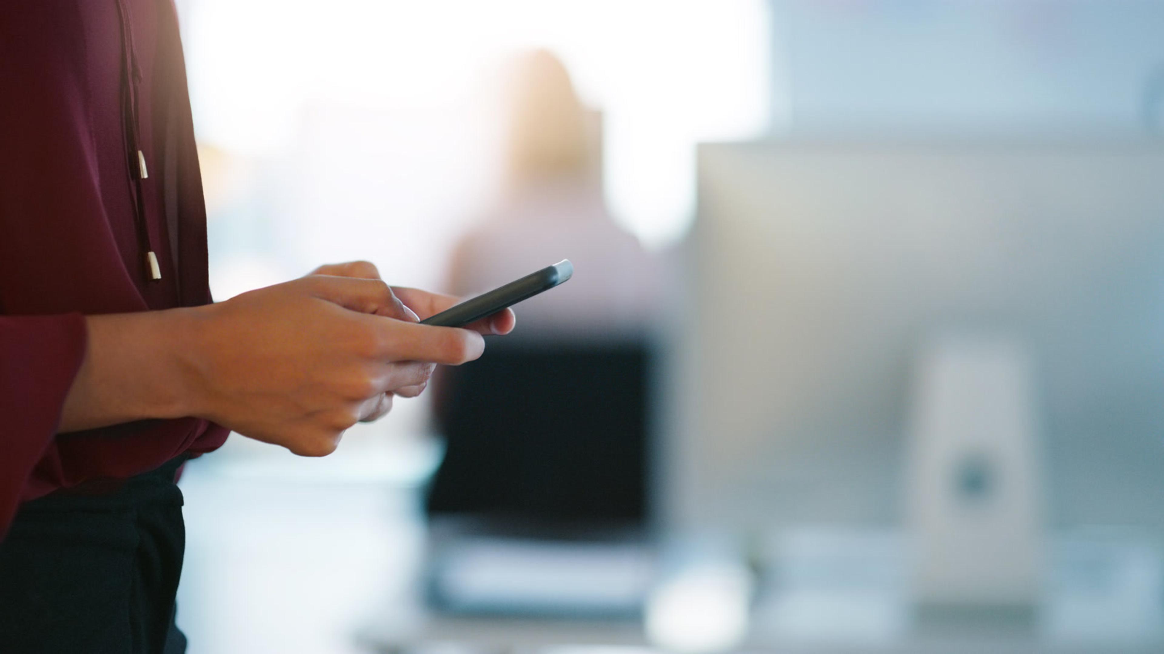 Professional woman texting on a smartphone in an office — BYOD softphone use