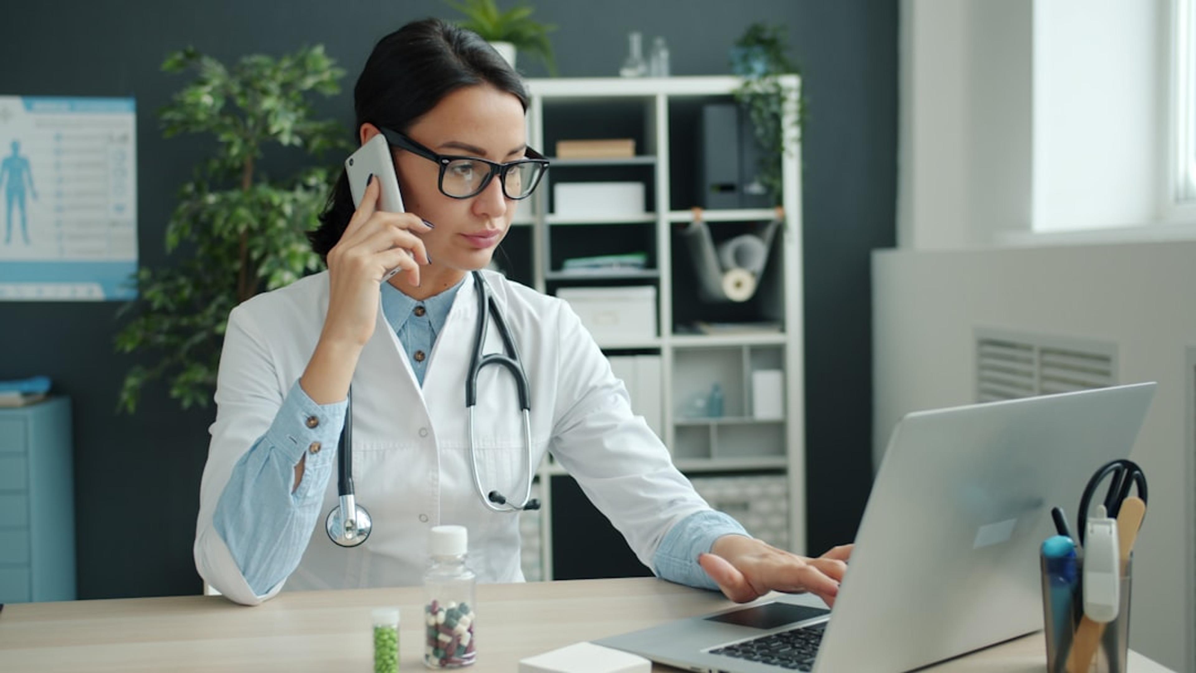 Doctor using a laptop and mobile phone in a clinic office