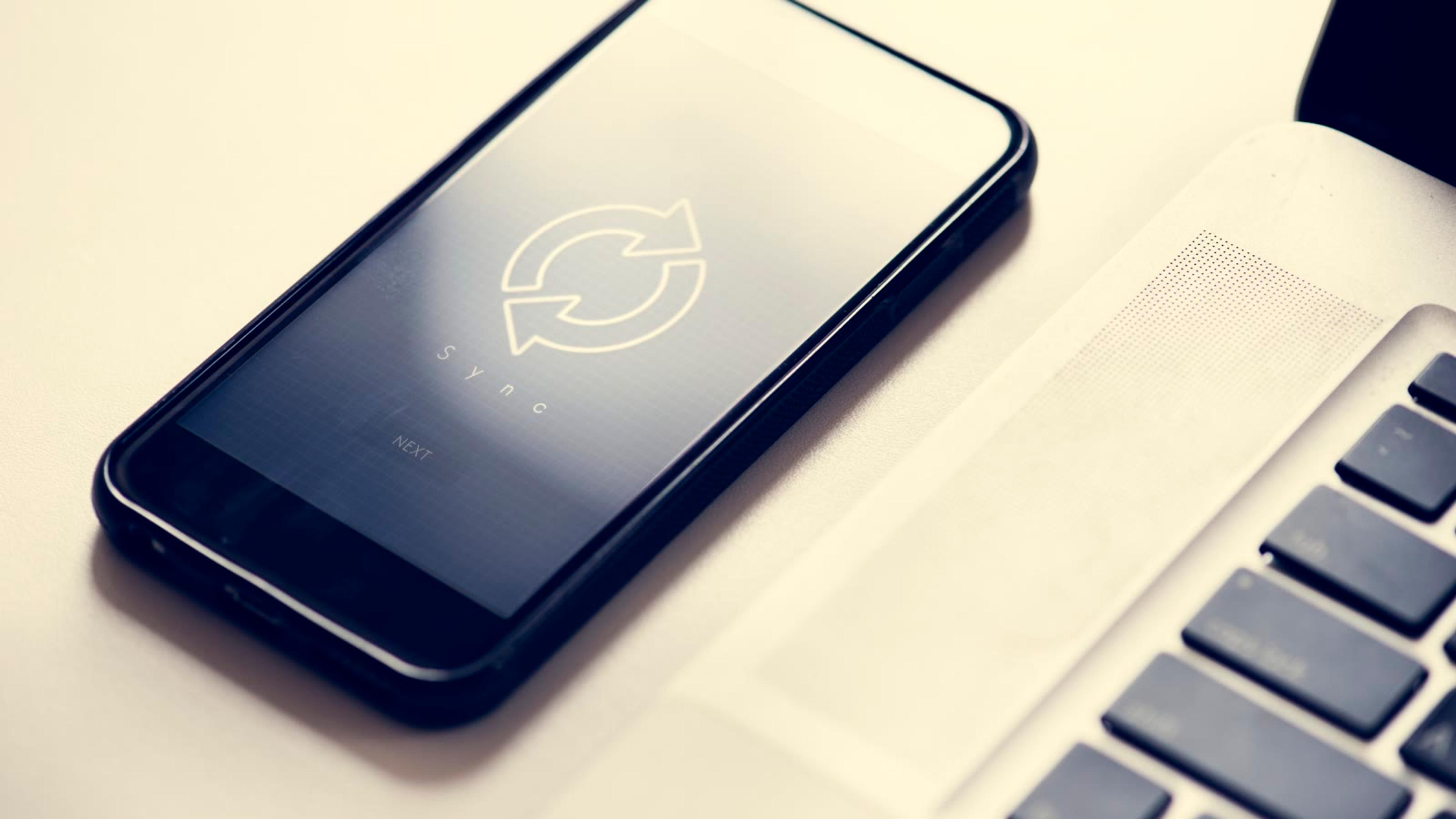 Smartphone showing a sync icon next to a laptop, as app logo branding reaches the apps on mobile and desktop