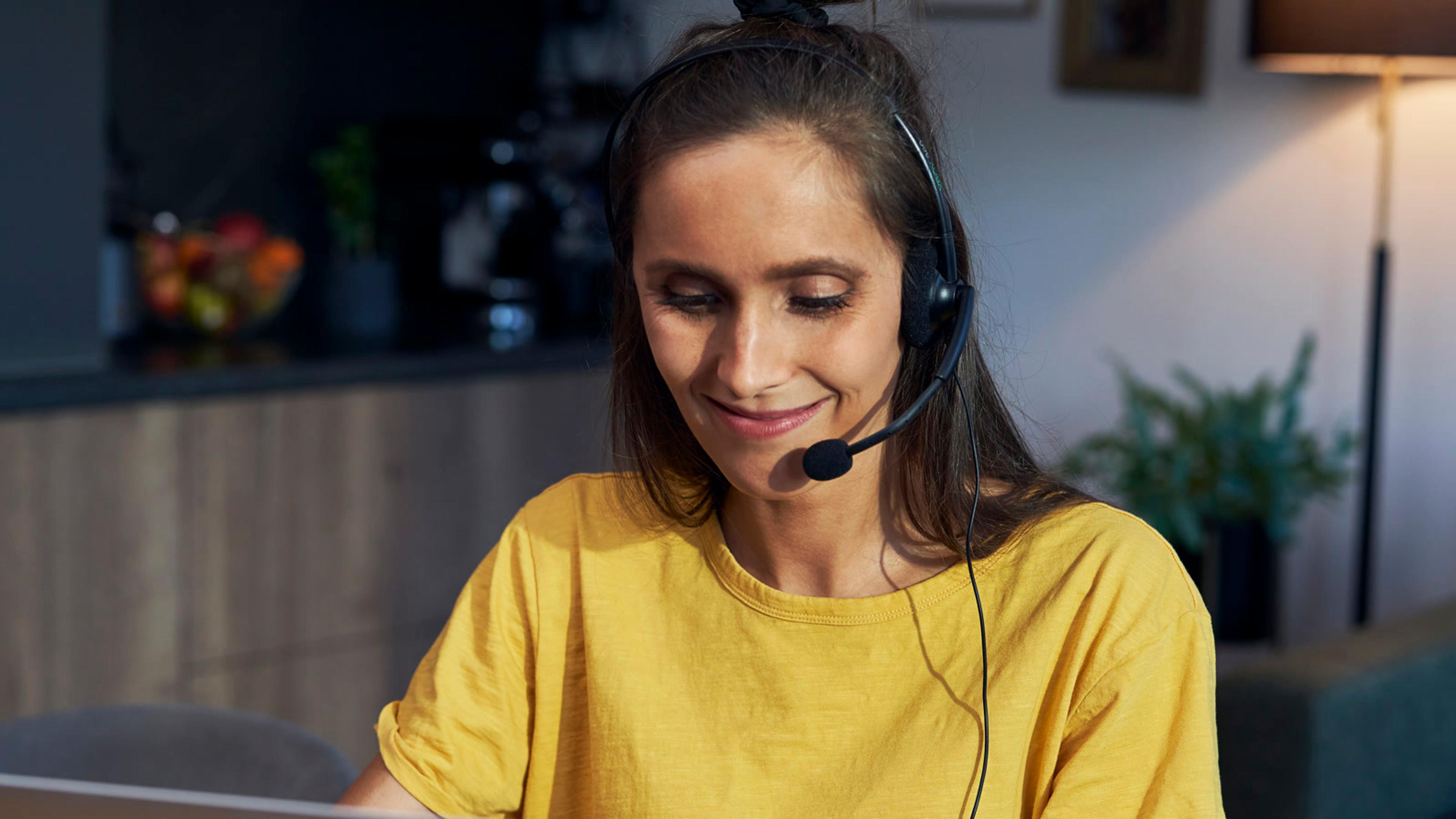 Woman with headset working at a laptop from home — mobile SIP softphone for Mitel teams